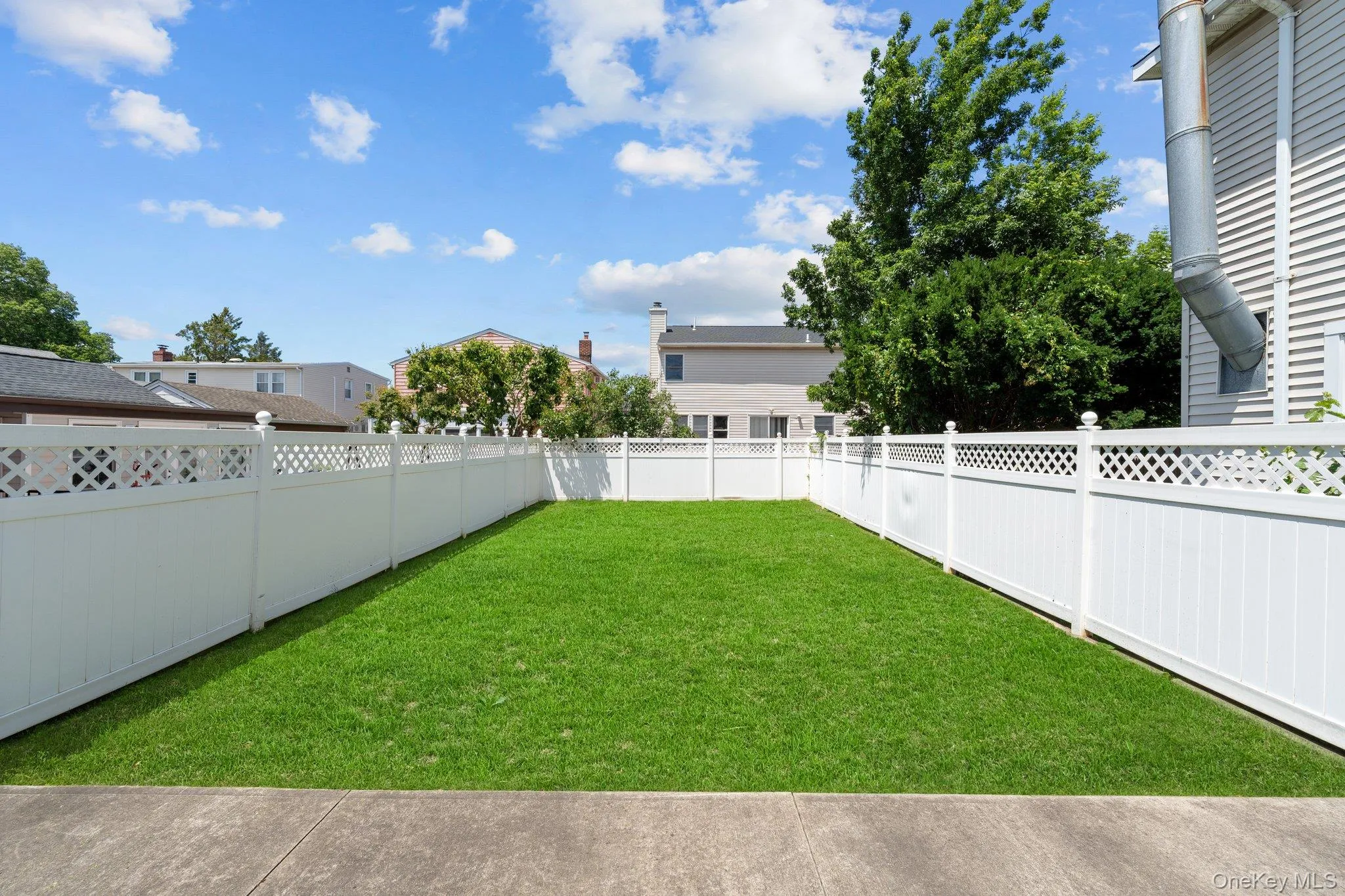 Expansive rear yard featuring a manicured lawn, full white privacy fencing with lattice accents, and a concrete patio Expansive rear yard featuring a manicured lawn, full white privacy fencing with lattice accents, and a concrete patio