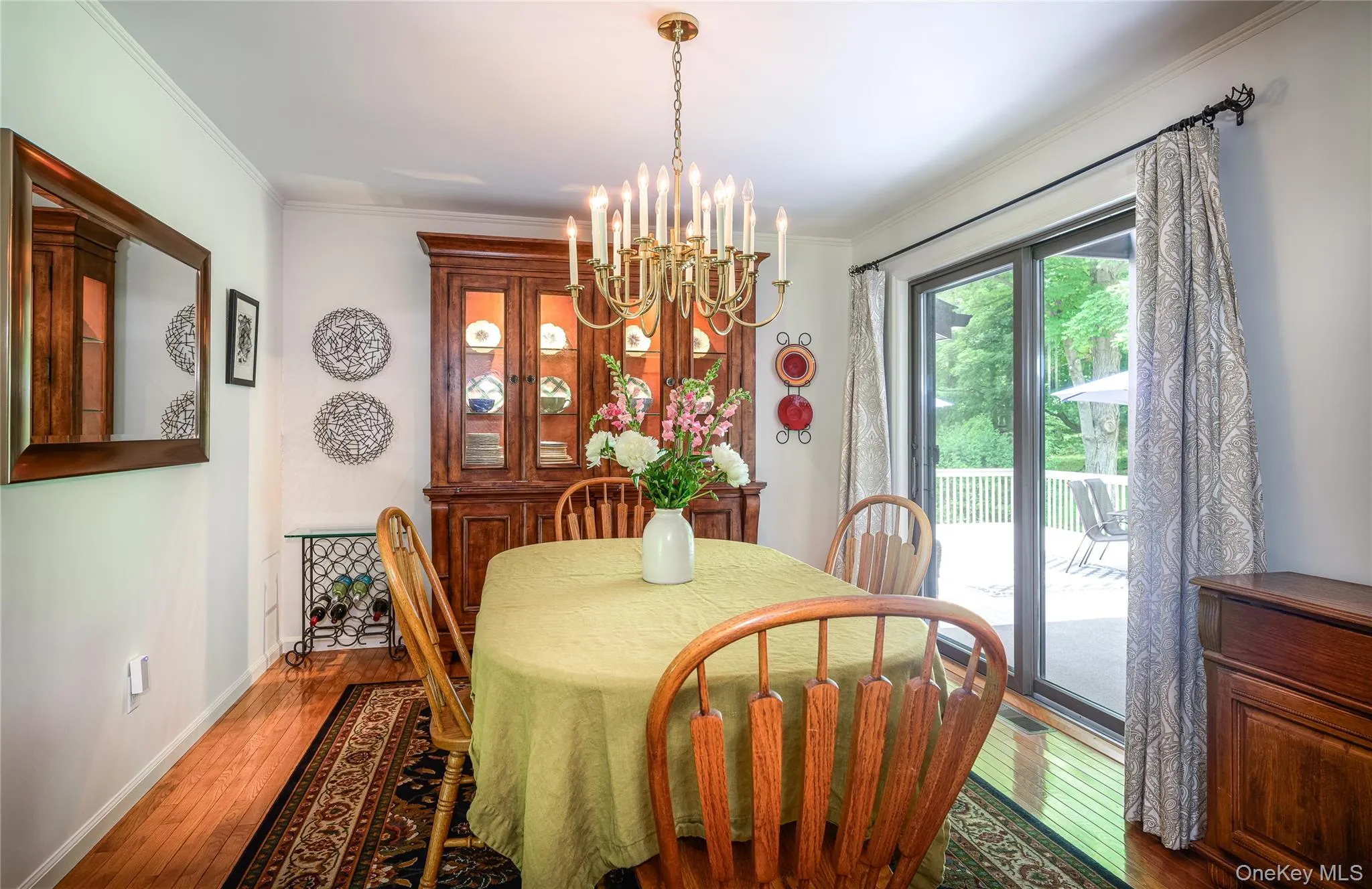 Dining area featuring wood-finish flooring, crown molding, a brass chandelier, and sliding glass doors opening to an outdoor deck Dining area featuring wood-finish flooring, crown molding, a brass chandelier, and sliding glass doors opening to an outdoor deck