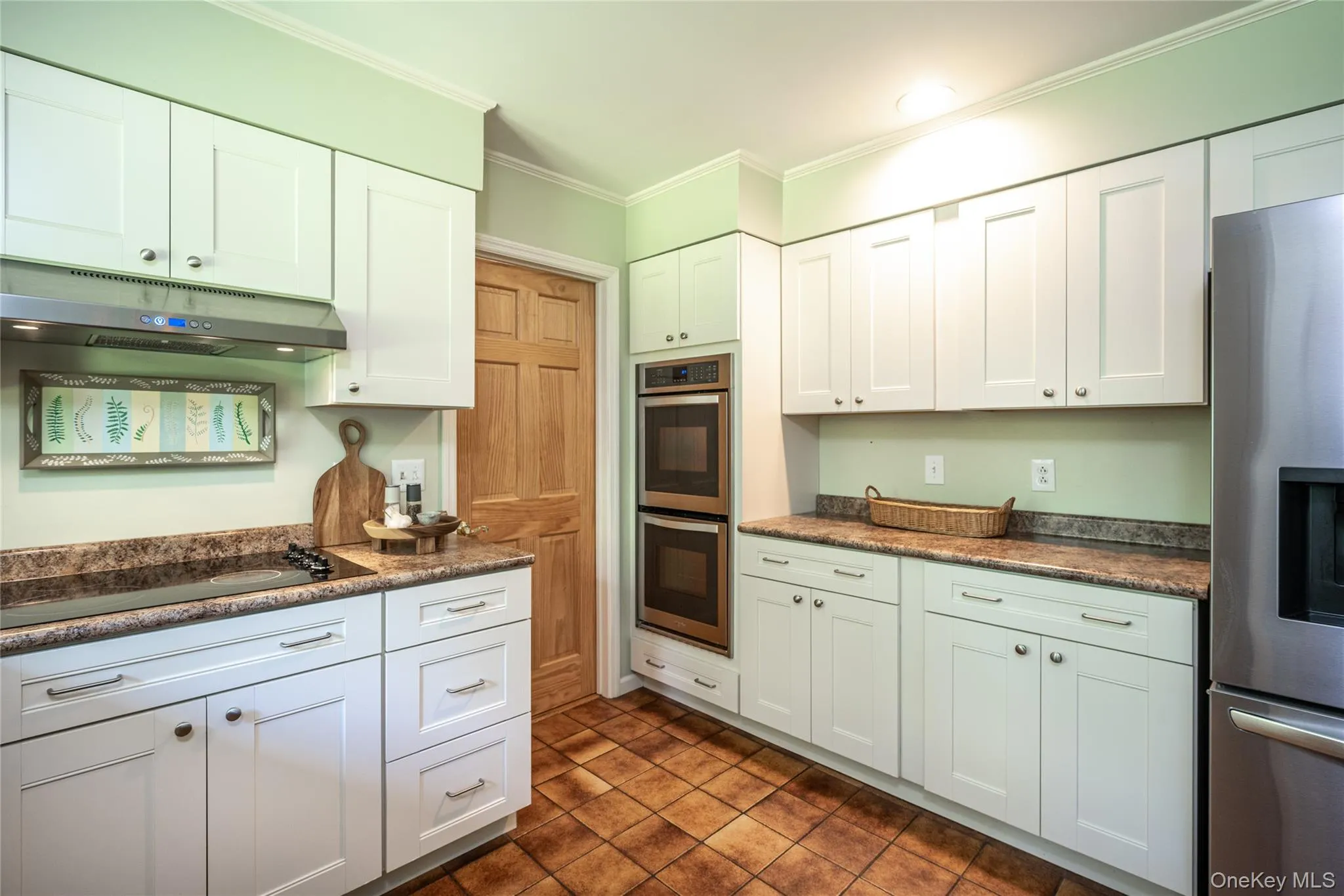 Kitchen featuring white cabinetry, built-in double ovens, stainless steel refrigerator, cooktop, and tile flooring Kitchen featuring white cabinetry, built-in double ovens, stainless steel refrigerator, cooktop, and tile flooring
