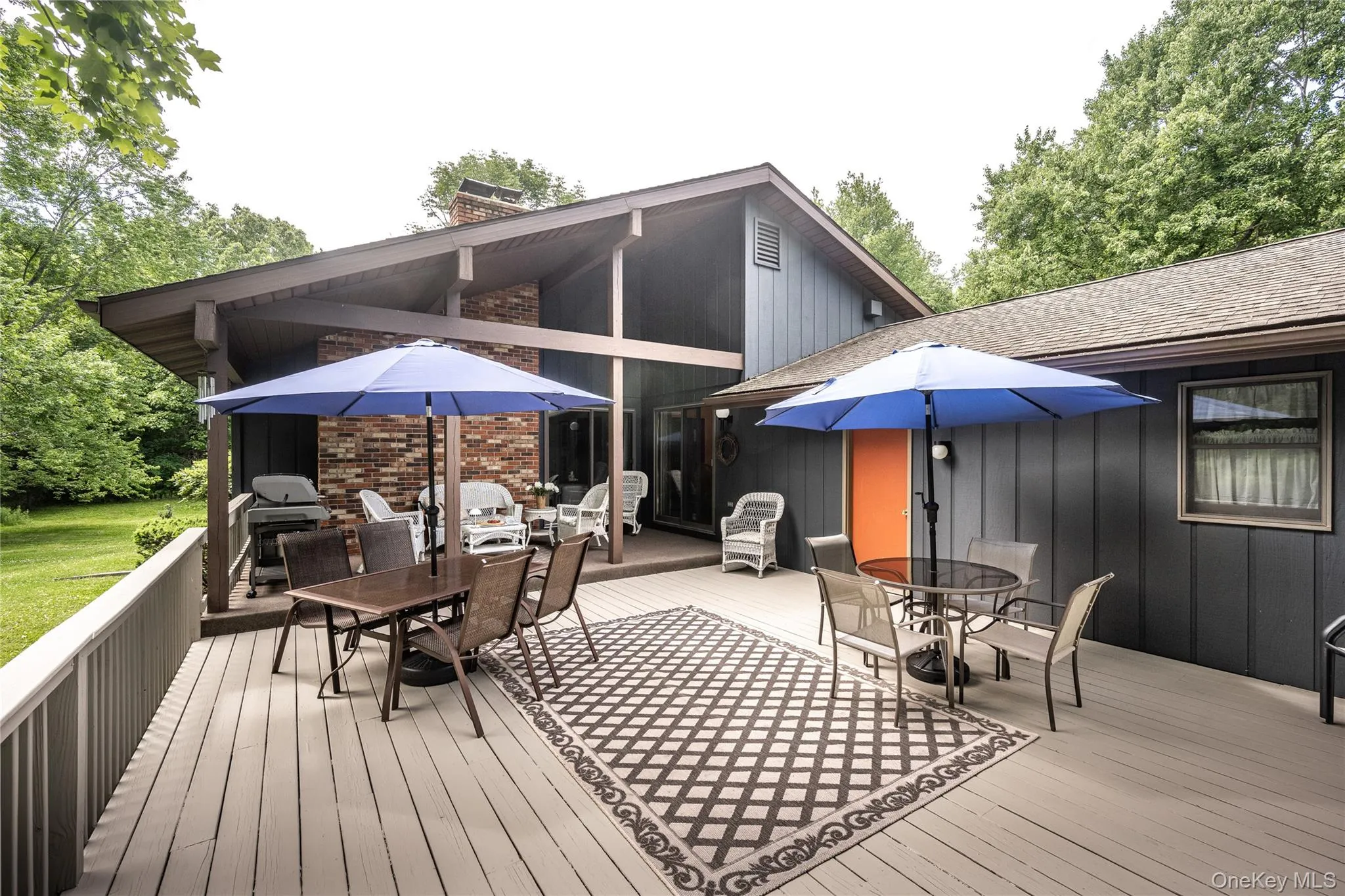 Expansive outdoor wood-finish deck with a prominent brick chimney, charcoal vertical siding, and a contrasting orange door Expansive outdoor wood-finish deck with a prominent brick chimney, charcoal vertical siding, and a contrasting orange door