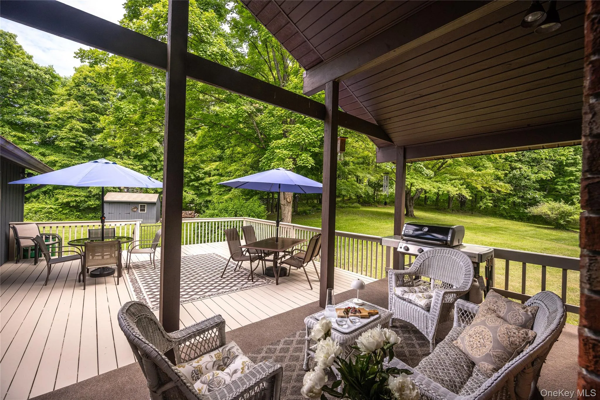 Expansive covered deck featuring a wood-finish ceiling, exposed structural beams, and a light-colored deck surface Expansive covered deck featuring a wood-finish ceiling, exposed structural beams, and a light-colored deck surface