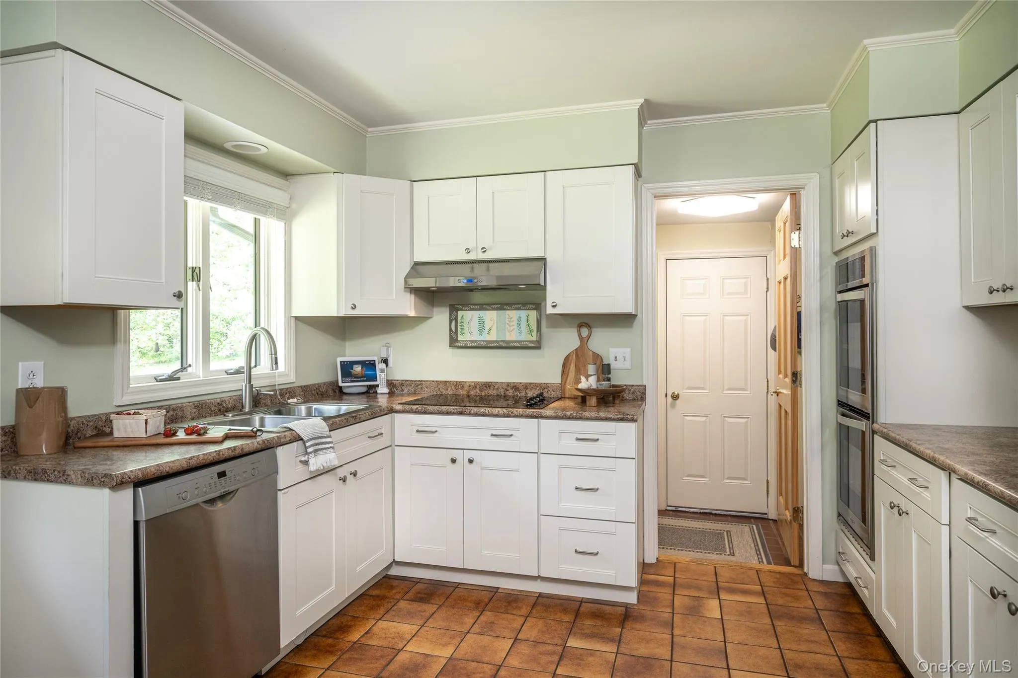 Kitchen featuring white shaker-style cabinetry, a stainless steel double-basin sink with a gooseneck faucet, integrated stainless steel dishwasher, double wall ovens, and tiled flooring Kitchen featuring white shaker-style cabinetry, a stainless steel double-basin sink with a gooseneck faucet, integrated stainless steel dishwasher, double wall ovens, and tiled flooring