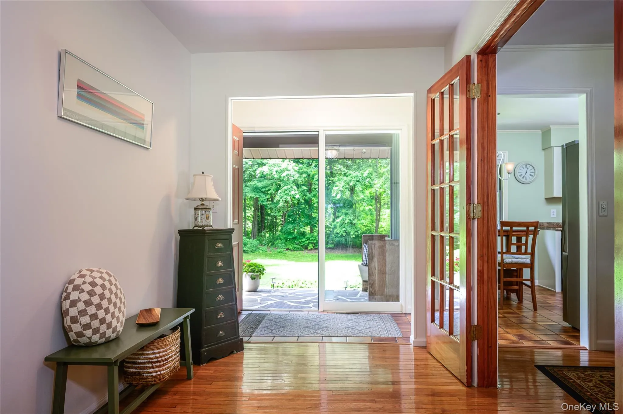 Hardwood flooring throughout the entry, double French doors with glass panels, and sliding glass doors revealing a stone patio and lush landscaping Hardwood flooring throughout the entry, double French doors with glass panels, and sliding glass doors revealing a stone patio and lush landscaping