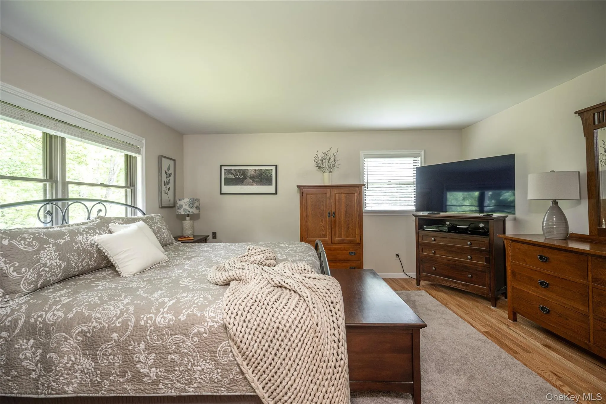 Bedroom featuring light neutral wall tones, wood-finish flooring, and multiple windows with natural light Bedroom featuring light neutral wall tones, wood-finish flooring, and multiple windows with natural light