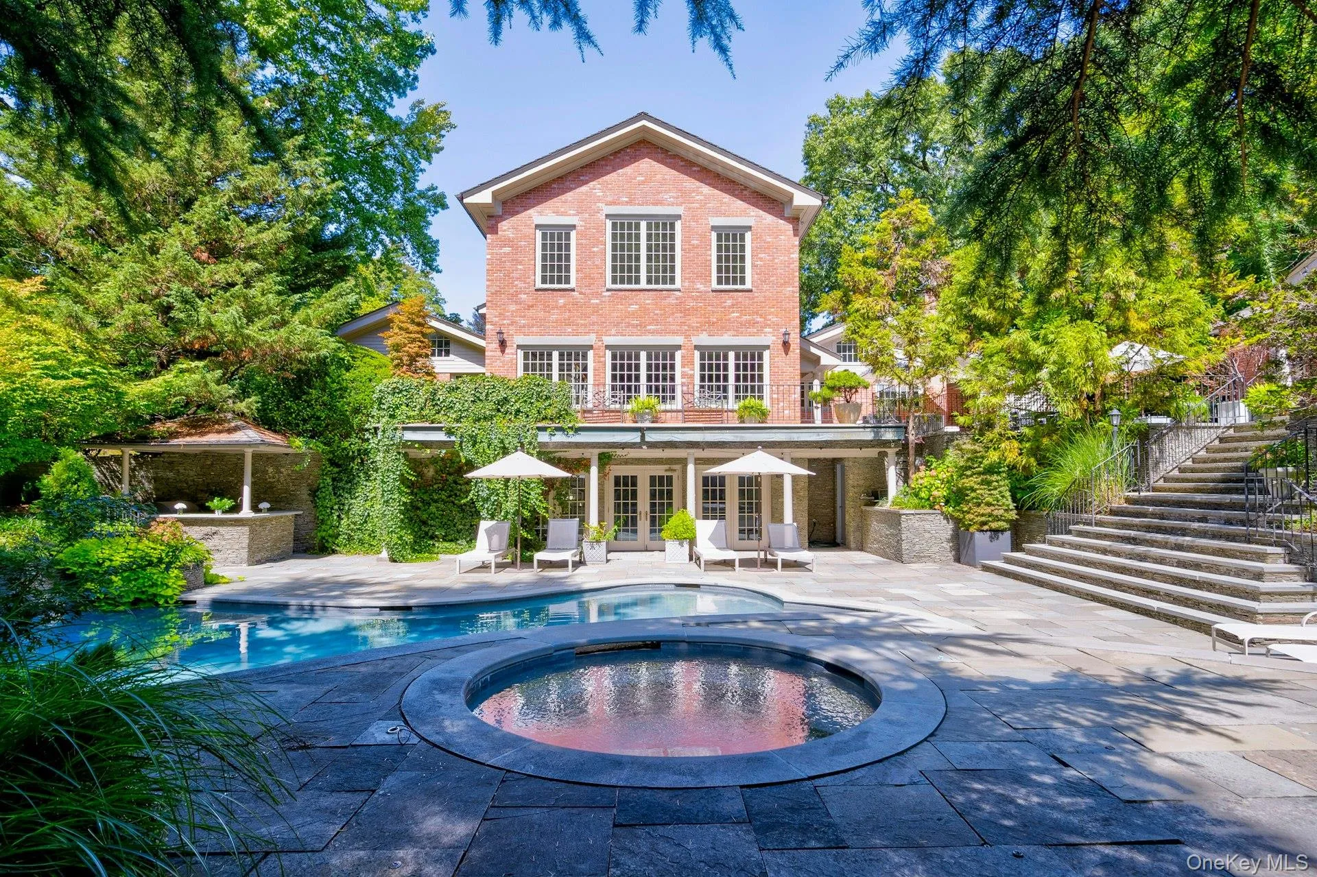 Back of house featuring french doors, stairway, a patio area, brick siding, and a pool with connected hot tub Back of house featuring french doors, stairway, a patio area, brick siding, and a pool with connected hot tub