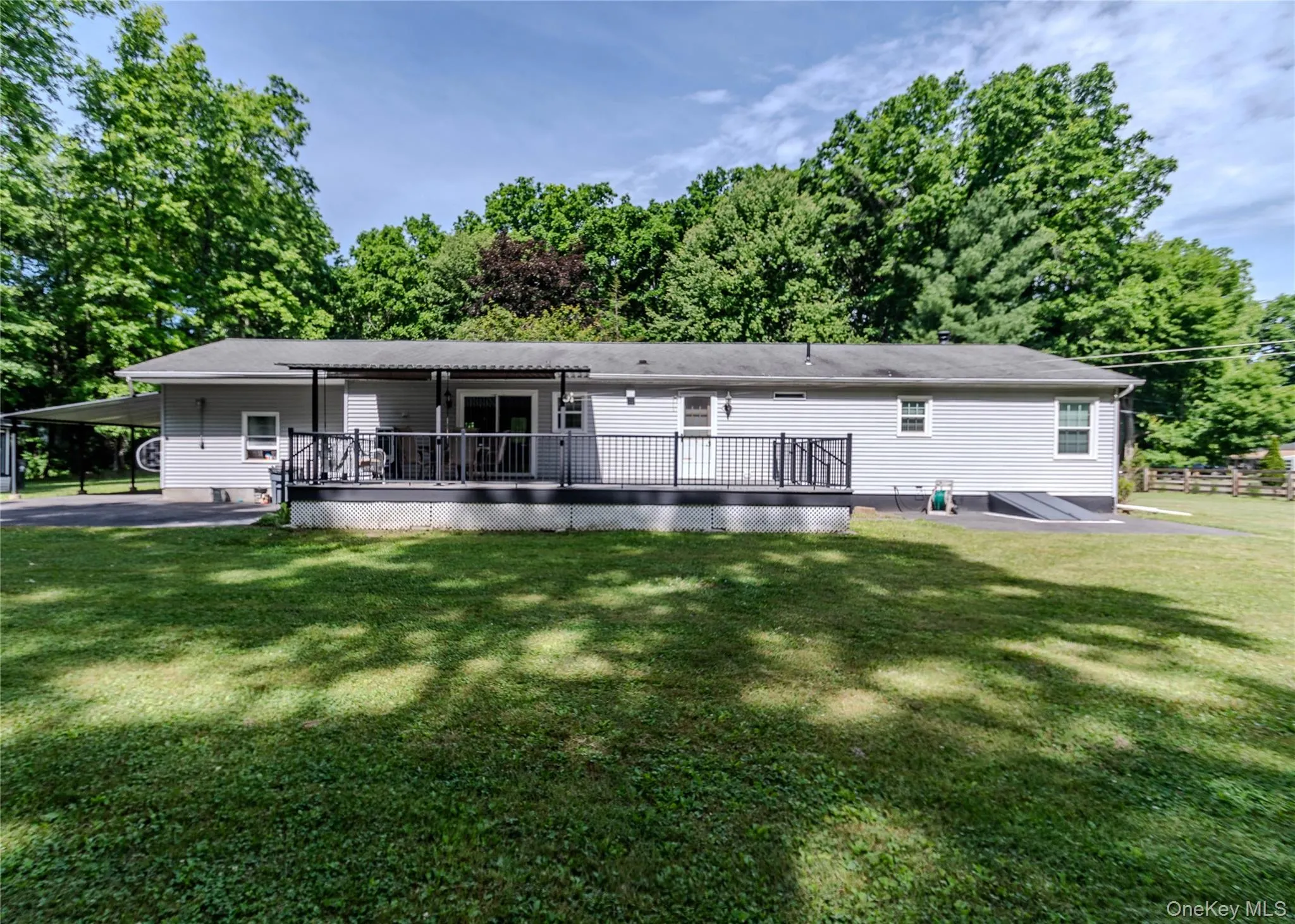 Rear exterior featuring light gray siding, a spacious elevated deck with black railings, a covered patio area, and a carport Rear exterior featuring light gray siding, a spacious elevated deck with black railings, a covered patio area, and a carport