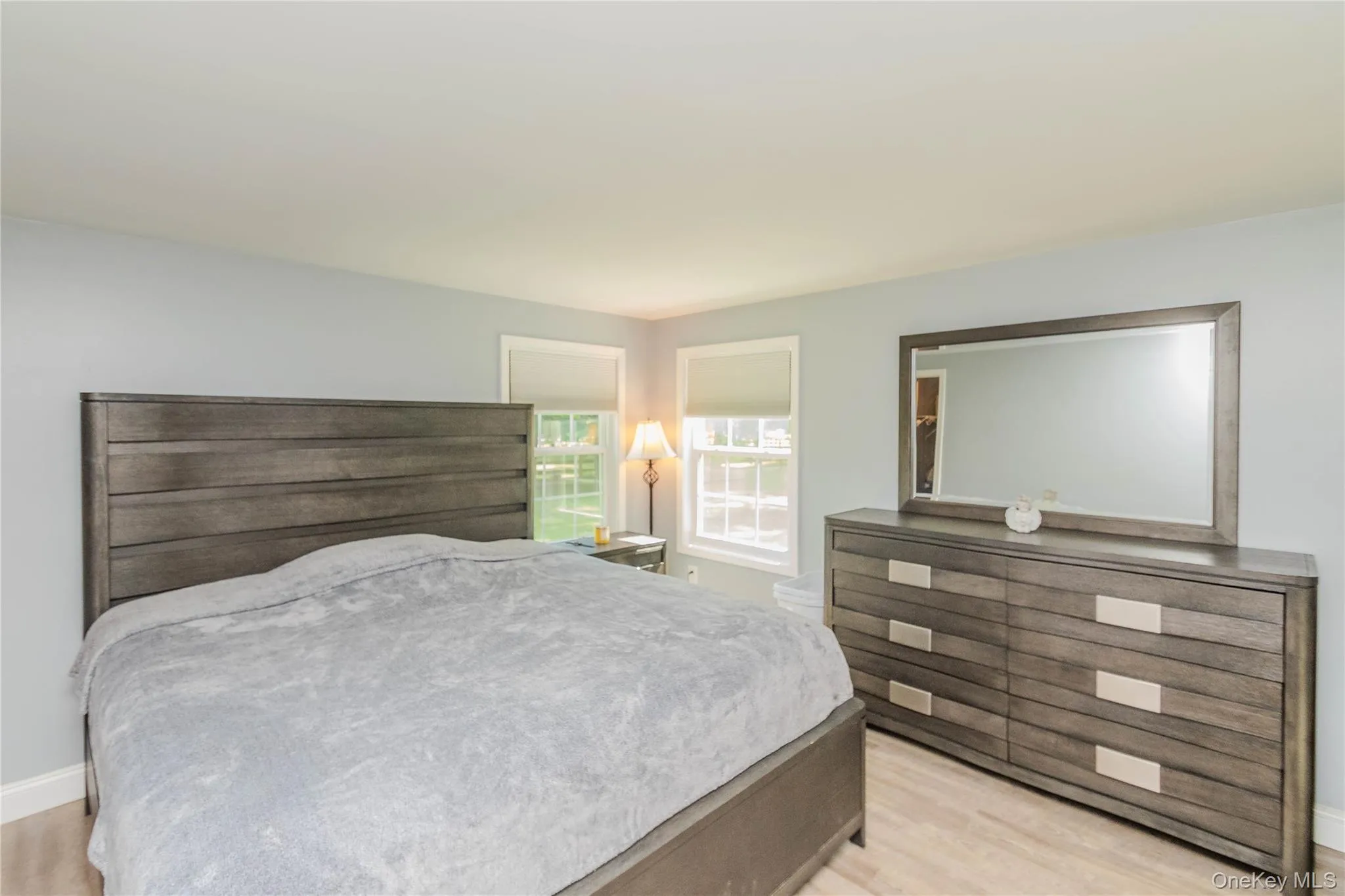 Bedroom featuring light wood-finish flooring and two windows with roller shades Bedroom featuring light wood-finish flooring and two windows with roller shades