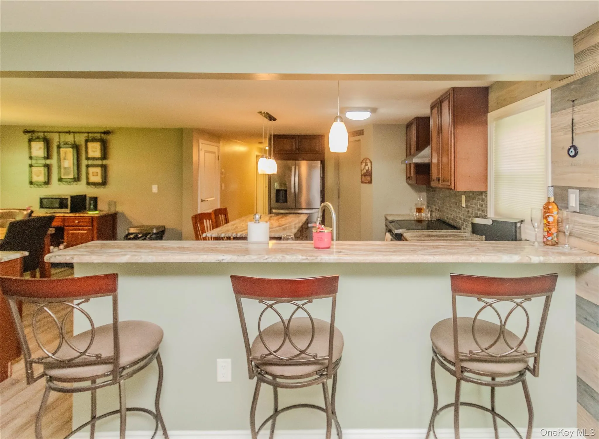 Kitchen featuring an extended breakfast bar with stone-finish countertop, wood-finish cabinetry, stainless steel appliances, and a mosaic tile backsplash Kitchen featuring an extended breakfast bar with stone-finish countertop, wood-finish cabinetry, stainless steel appliances, and a mosaic tile backsplash