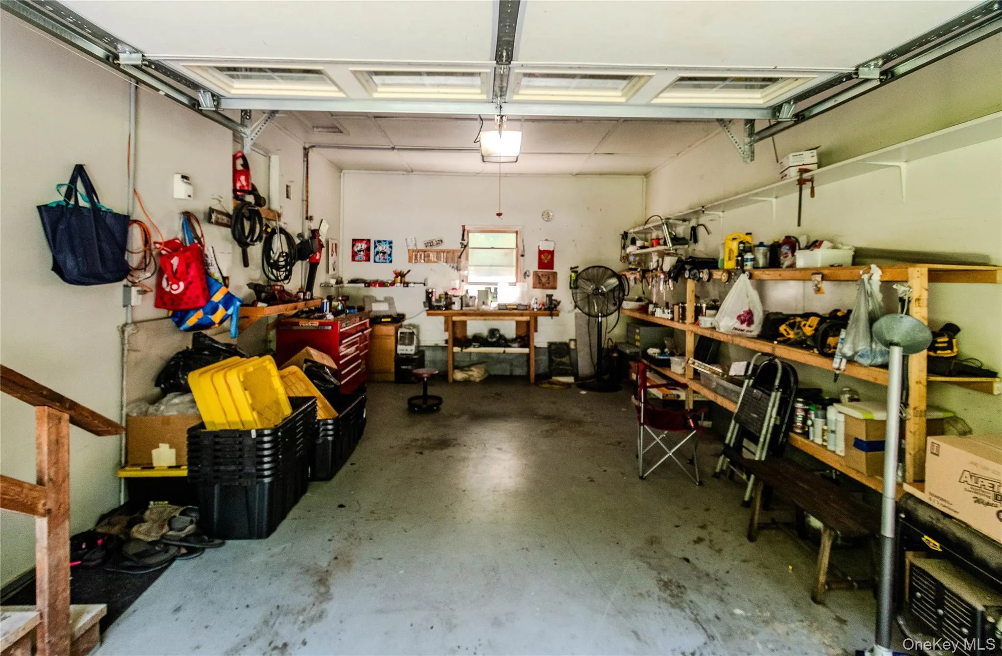 Spacious garage featuring a workshop area, built-in shelving, concrete flooring, and a window for natural light Spacious garage featuring a workshop area, built-in shelving, concrete flooring, and a window for natural light