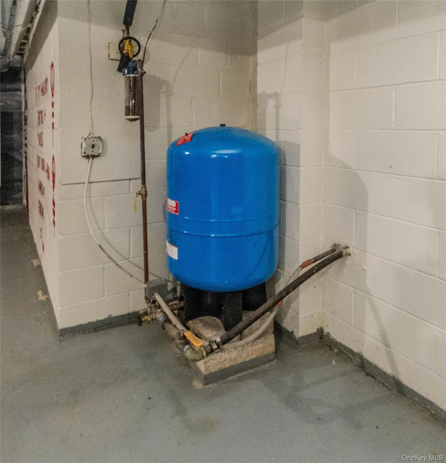 Well pressure tank system with associated plumbing, positioned against white painted concrete block walls Well pressure tank system with associated plumbing, positioned against white painted concrete block walls
