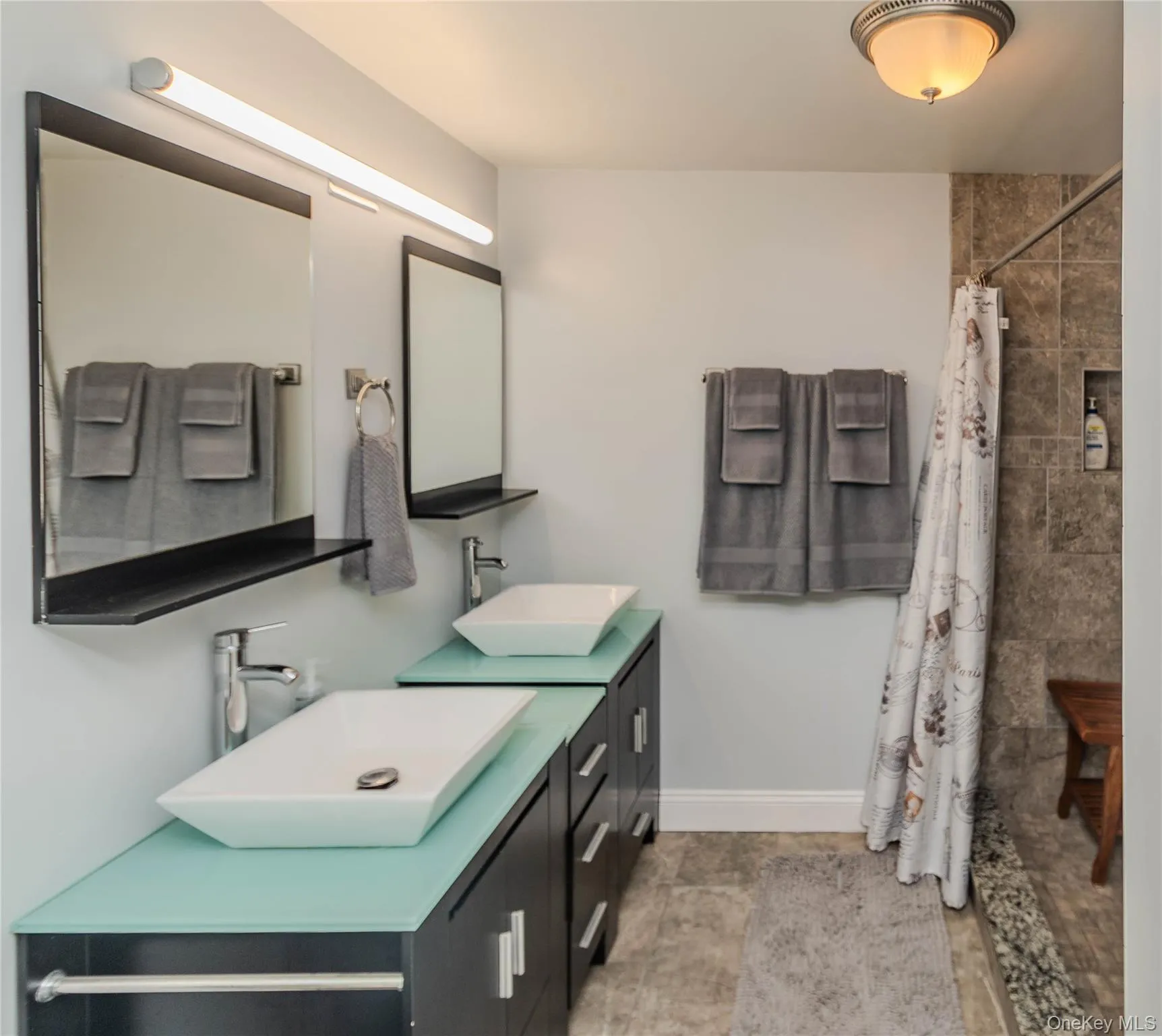 Dual vessel sinks with modern chrome faucets set on two separate vanities featuring light aqua glass countertops and dark cabinetry Dual vessel sinks with modern chrome faucets set on two separate vanities featuring light aqua glass countertops and dark cabinetry