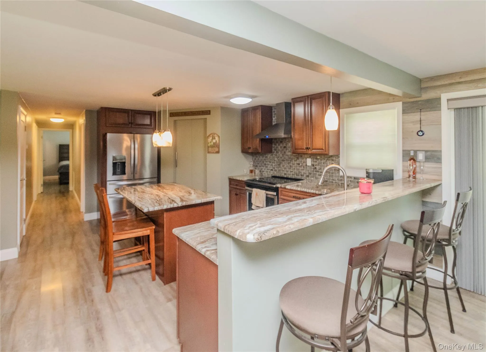 Kitchen featuring a multi-toned stone countertop island and breakfast bar, stainless steel appliances, wood cabinetry, and a mosaic tile backsplash Kitchen featuring a multi-toned stone countertop island and breakfast bar, stainless steel appliances, wood cabinetry, and a mosaic tile backsplash