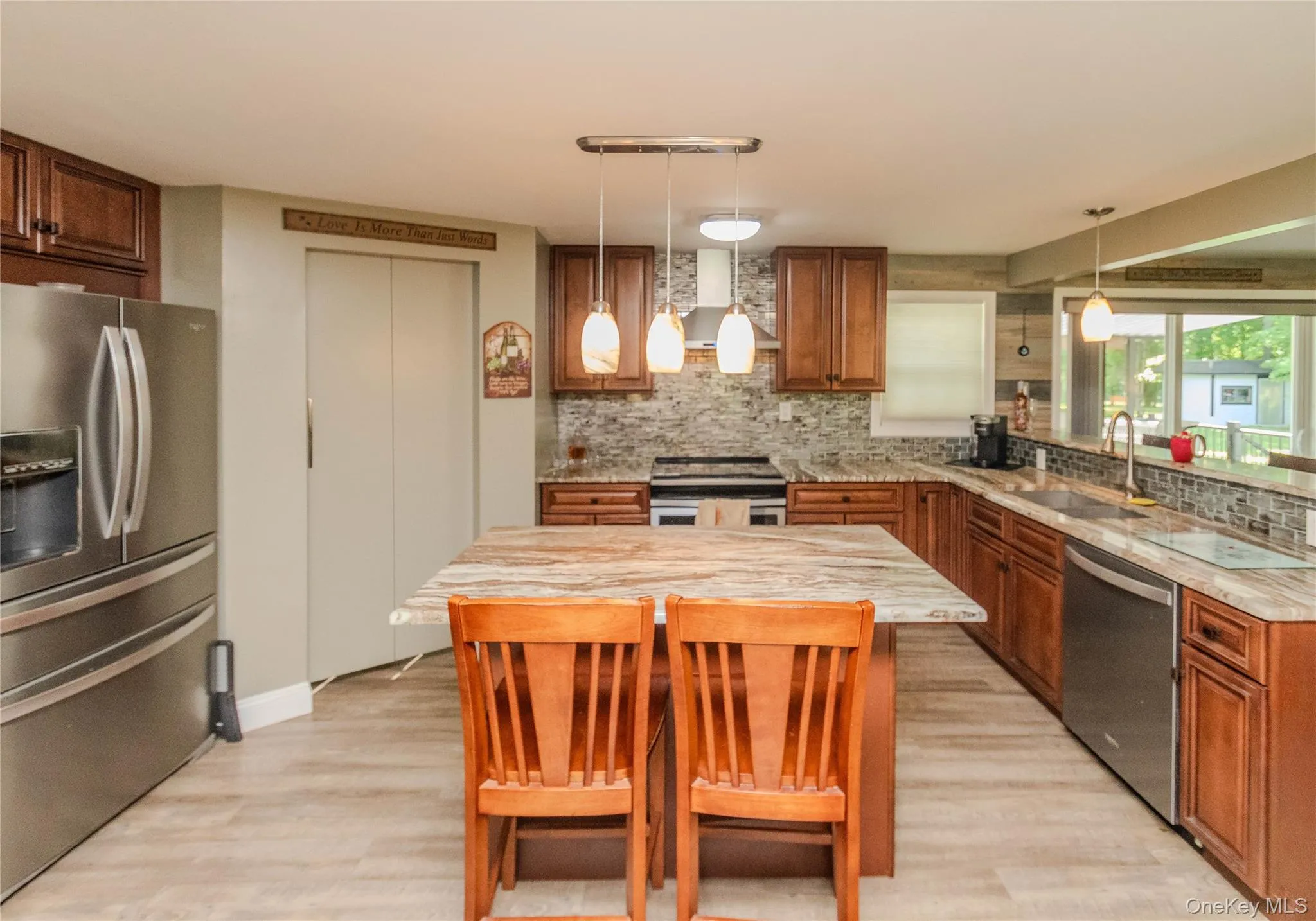 Kitchen featuring a large island with stone countertops, wood-finish flooring, stainless steel appliances, and wood cabinetry Kitchen featuring a large island with stone countertops, wood-finish flooring, stainless steel appliances, and wood cabinetry