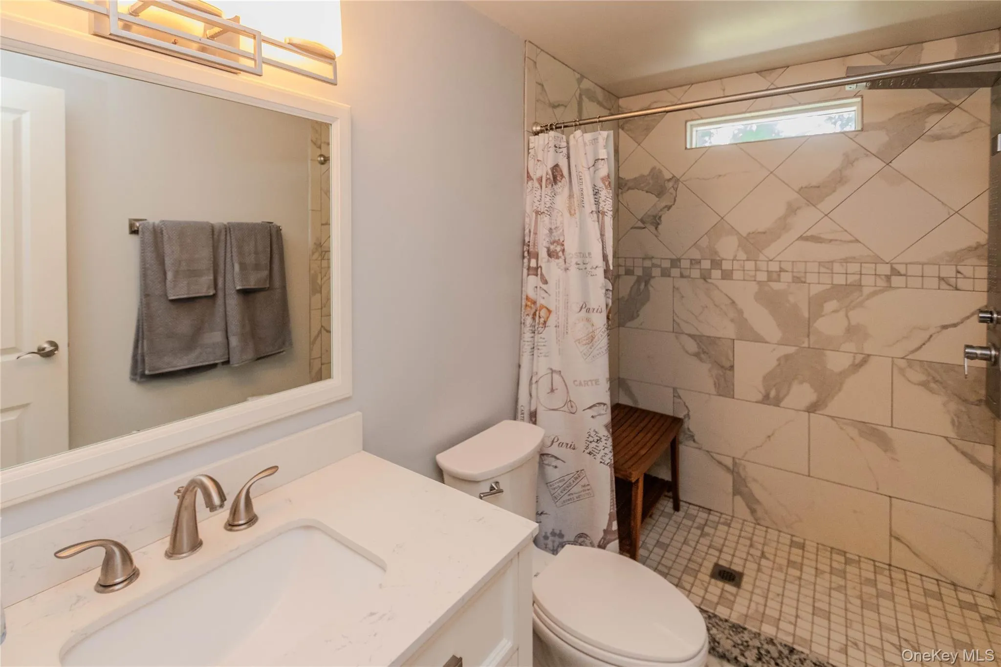 Bathroom featuring a built-in vanity with a white countertop and undermount sink, brushed nickel faucet, and a large framed mirror Bathroom featuring a built-in vanity with a white countertop and undermount sink, brushed nickel faucet, and a large framed mirror