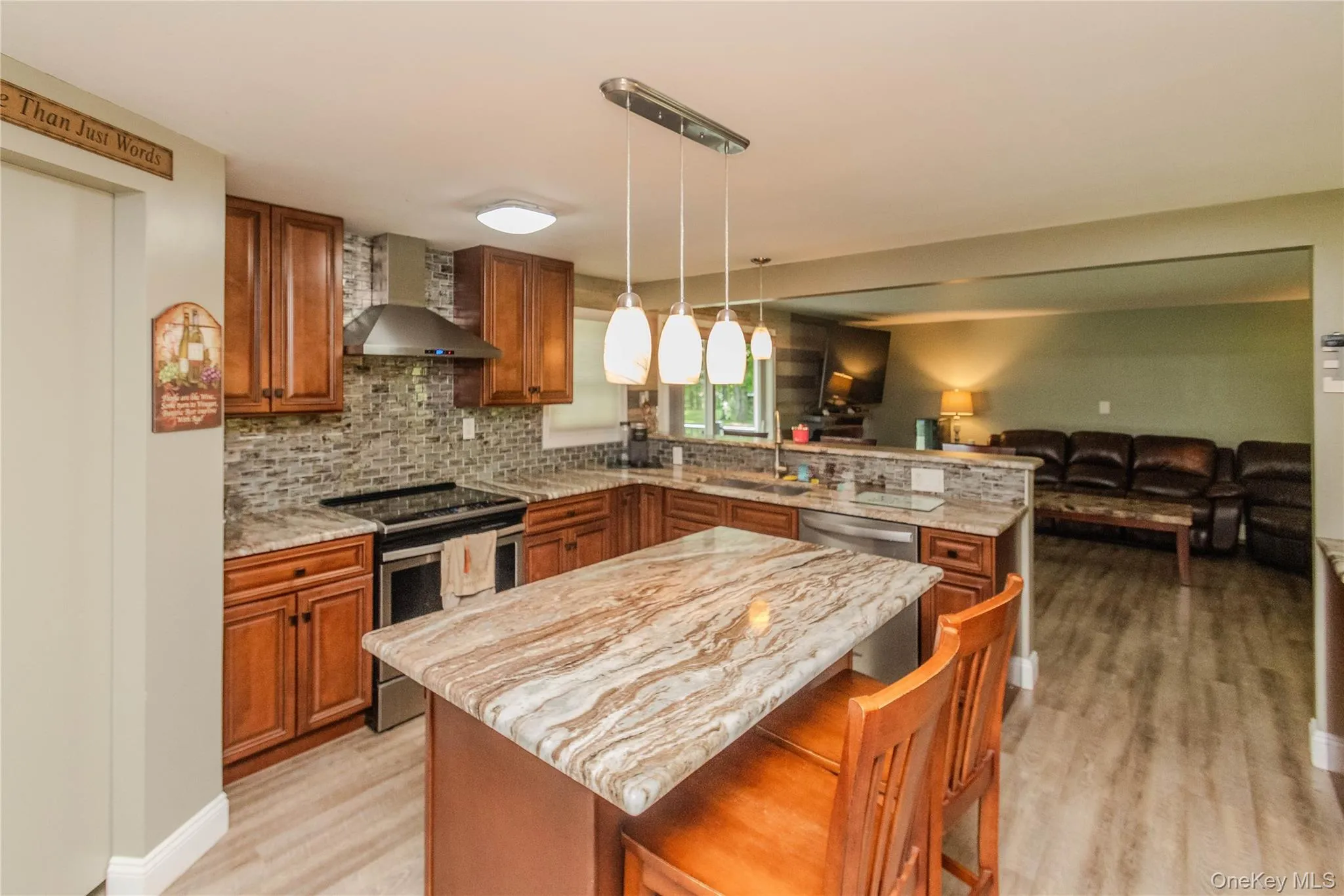 Kitchen featuring a large island with stone countertop, stainless steel appliances, stone tile backsplash, wood-finish flooring, and recessed lighting Kitchen featuring a large island with stone countertop, stainless steel appliances, stone tile backsplash, wood-finish flooring, and recessed lighting
