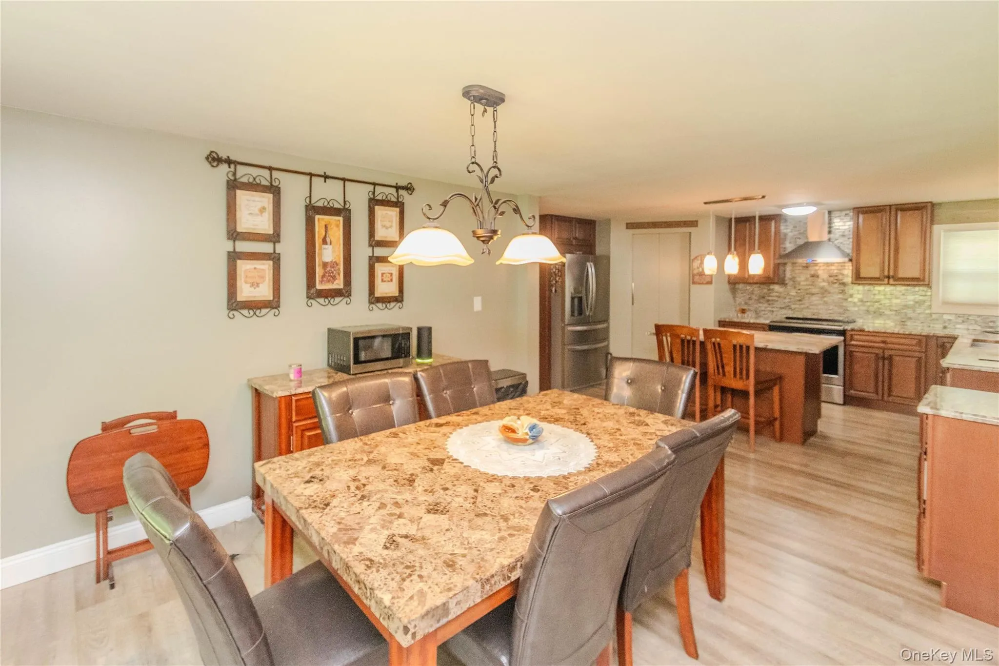 Open-concept dining area featuring a stone-look tabletop, wrought iron chandelier, and wood-finish flooring Open-concept dining area featuring a stone-look tabletop, wrought iron chandelier, and wood-finish flooring