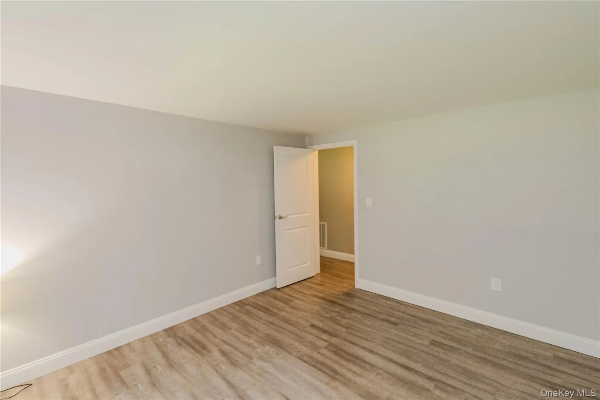 Interior room featuring light gray walls, wood-finish flooring, white baseboards, and a white interior door Interior room featuring light gray walls, wood-finish flooring, white baseboards, and a white interior door