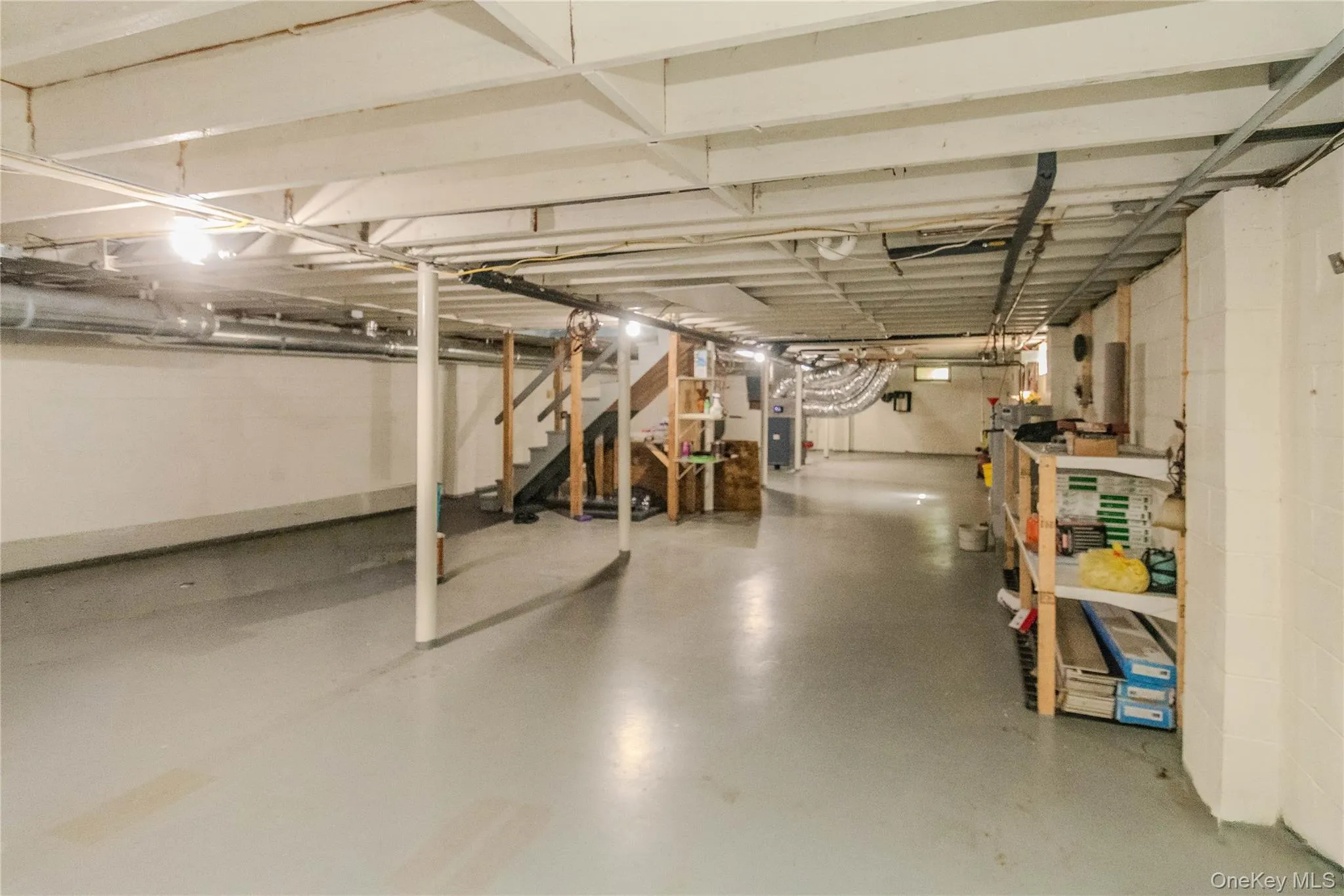 Spacious lower level featuring a painted concrete floor, exposed joist ceiling, and a visible staircase Spacious lower level featuring a painted concrete floor, exposed joist ceiling, and a visible staircase