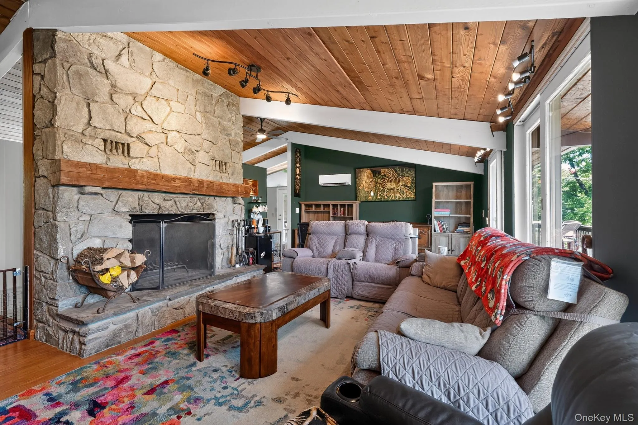 Great room featuring a full-height natural stone fireplace, exposed beam wood-finish ceiling, track lighting, and a ductless mini-split system Great room featuring a full-height natural stone fireplace, exposed beam wood-finish ceiling, track lighting, and a ductless mini-split system