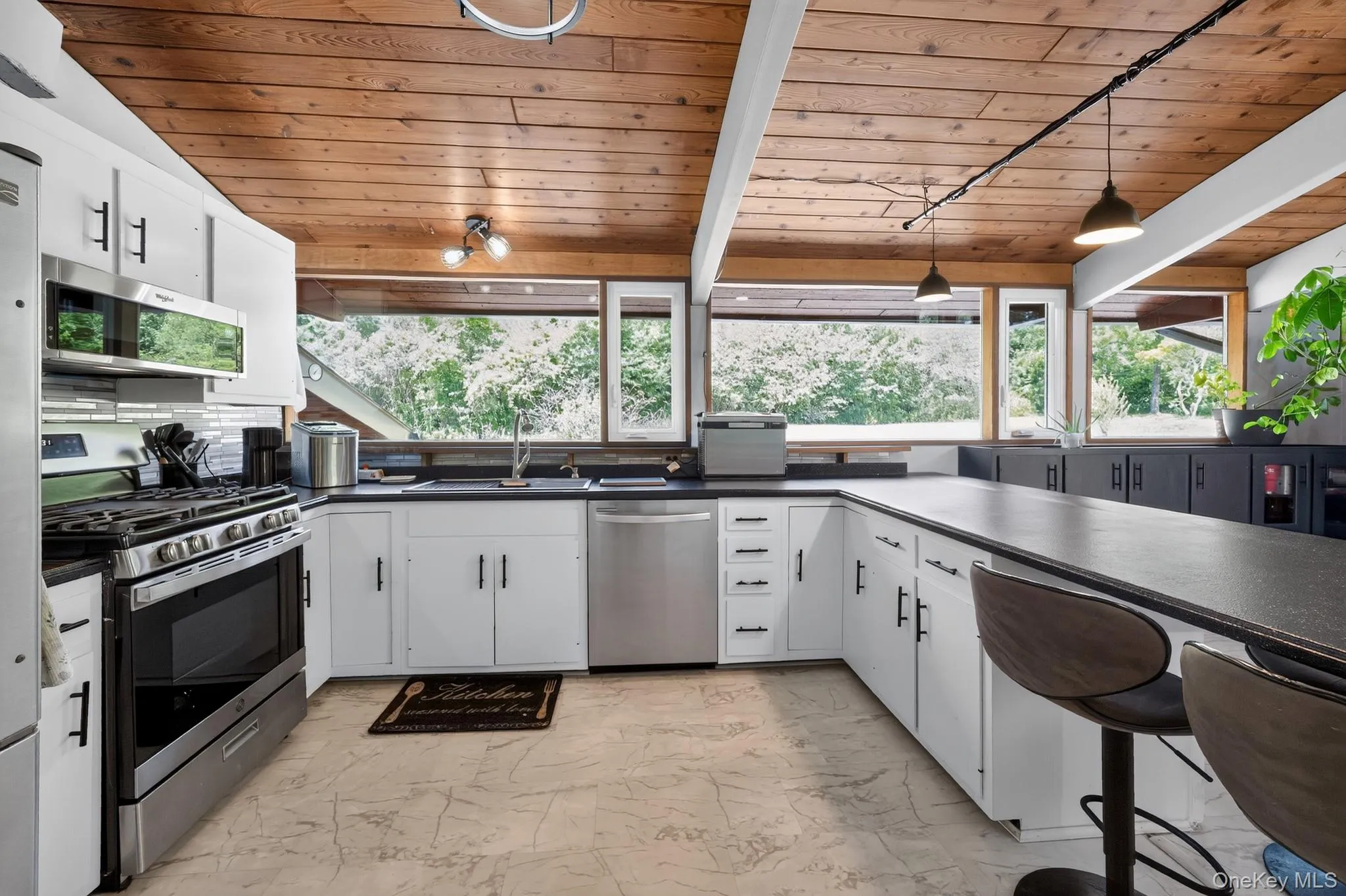 Kitchen featuring a wood plank ceiling with exposed beams, white cabinetry, dark countertops, stainless steel appliances, and a tile backsplash Kitchen featuring a wood plank ceiling with exposed beams, white cabinetry, dark countertops, stainless steel appliances, and a tile backsplash