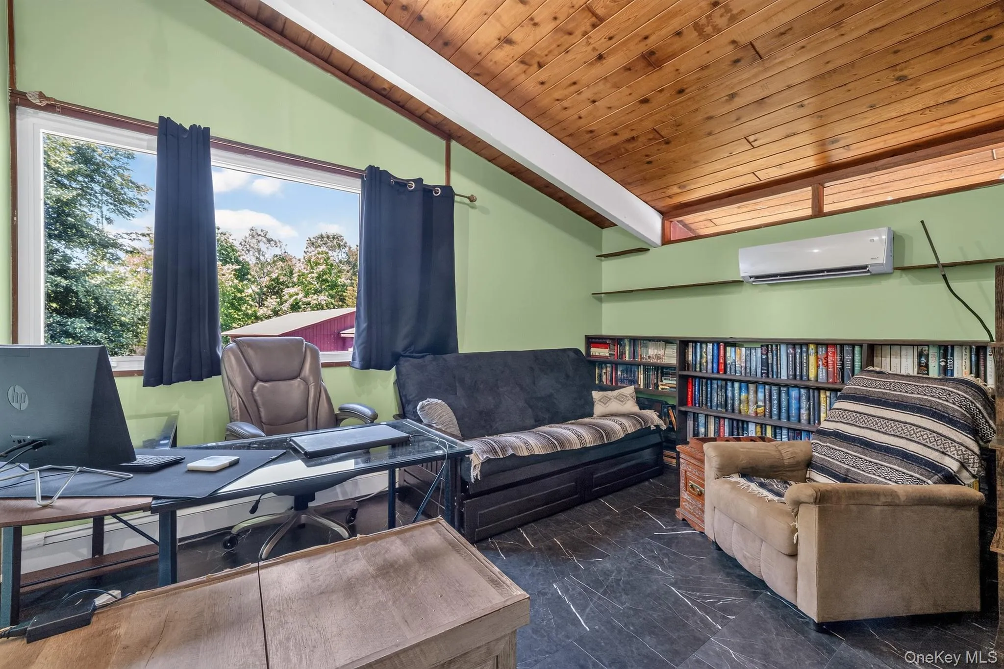 Vaulted wood-paneled ceiling with exposed beams, large picture window with outdoor scenery, full-wall built-in shelving, slate-look flooring, and a wall-mounted mini-split system Vaulted wood-paneled ceiling with exposed beams, large picture window with outdoor scenery, full-wall built-in shelving, slate-look flooring, and a wall-mounted mini-split system