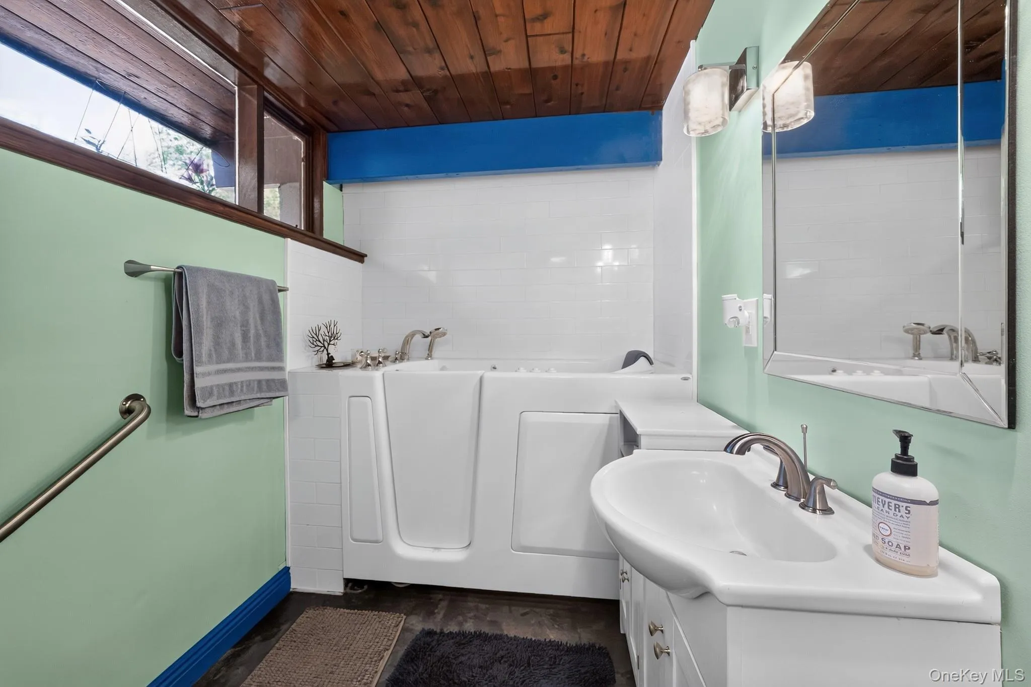 Bathroom featuring a walk-in tub, white subway tile surround, wood-finish ceiling, and an integrated vanity sink with storage Bathroom featuring a walk-in tub, white subway tile surround, wood-finish ceiling, and an integrated vanity sink with storage