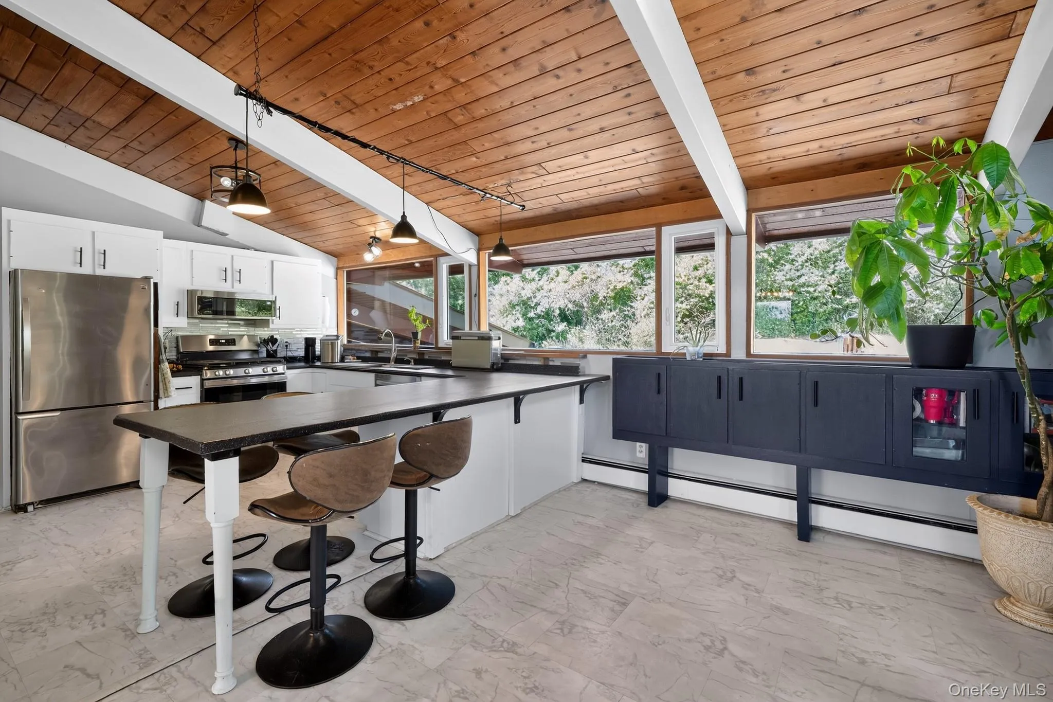 Kitchen featuring a vaulted wood-paneled ceiling with exposed beams, white cabinetry, stainless steel appliances, and a large central island with seating Kitchen featuring a vaulted wood-paneled ceiling with exposed beams, white cabinetry, stainless steel appliances, and a large central island with seating