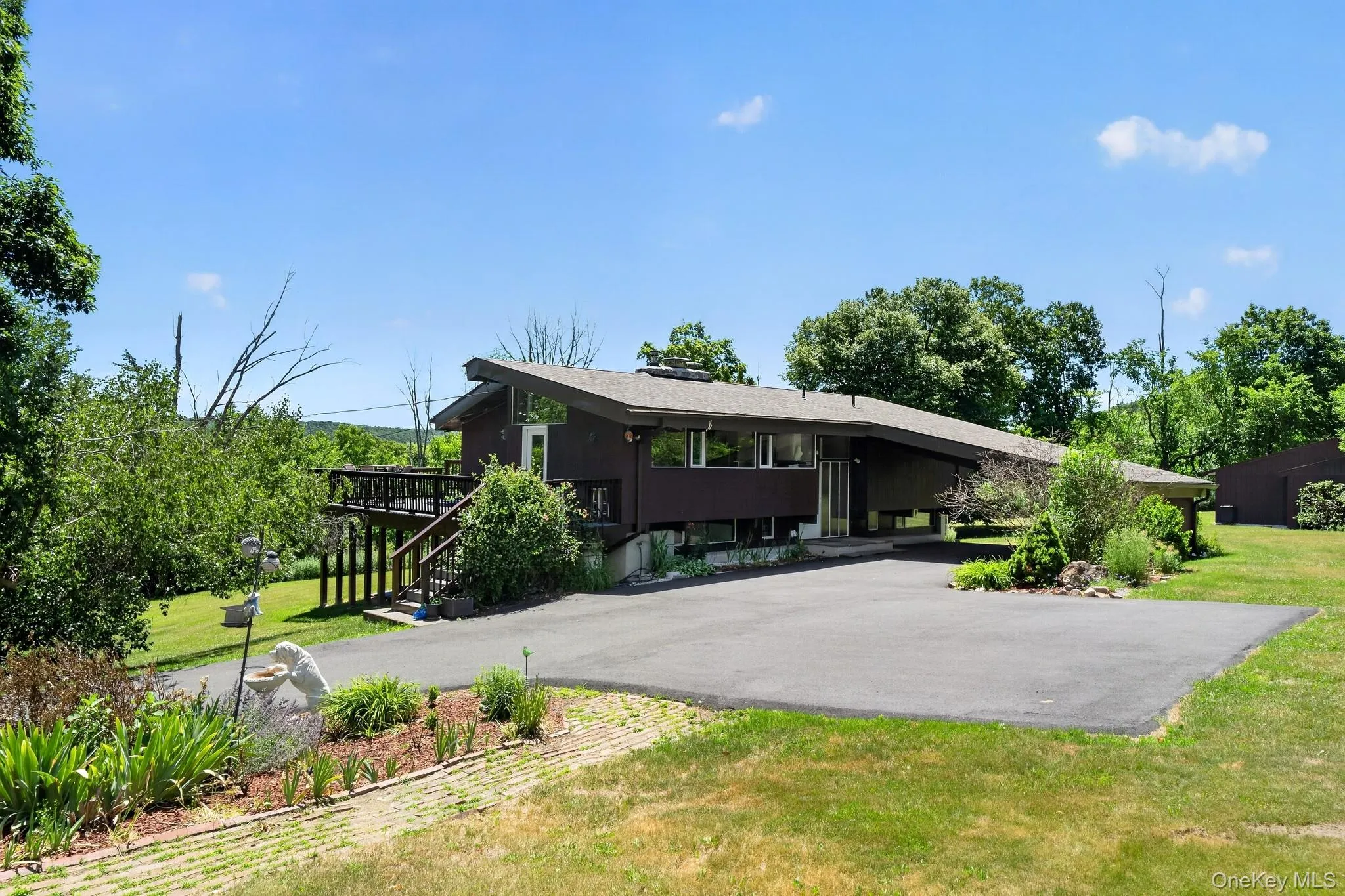 Contemporary architecture featuring a dark brown exterior, expansive asphalt driveway, and an elevated deck with wood railing Contemporary architecture featuring a dark brown exterior, expansive asphalt driveway, and an elevated deck with wood railing