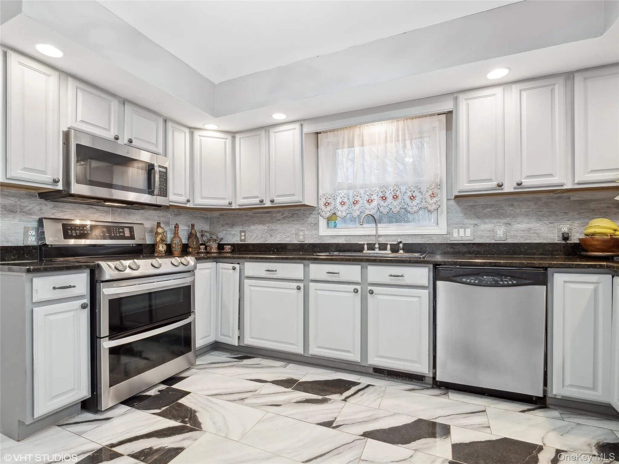Kitchen with decorative backsplash, white cabinetry, sink, and stainless steel appliances Kitchen with decorative backsplash, white cabinetry, sink, and stainless steel appliances
