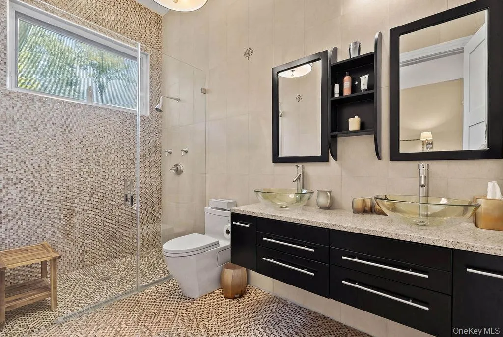 Spacious bathroom featuring a dual vanity with vessel sinks, a large shower with mosaic tile, pebble flooring, and a transom window Spacious bathroom featuring a dual vanity with vessel sinks, a large shower with mosaic tile, pebble flooring, and a transom window