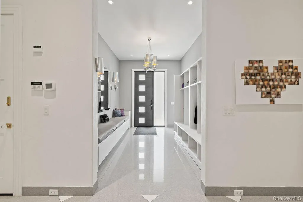 Spacious side entrance foyer featuring light-toned flooring, recessed lighting, a modern chandelier, integrated built-in storage, and a built-in bench with cushioned seating Spacious side entrance foyer featuring light-toned flooring, recessed lighting, a modern chandelier, integrated built-in storage, and a built-in bench with cushioned seating