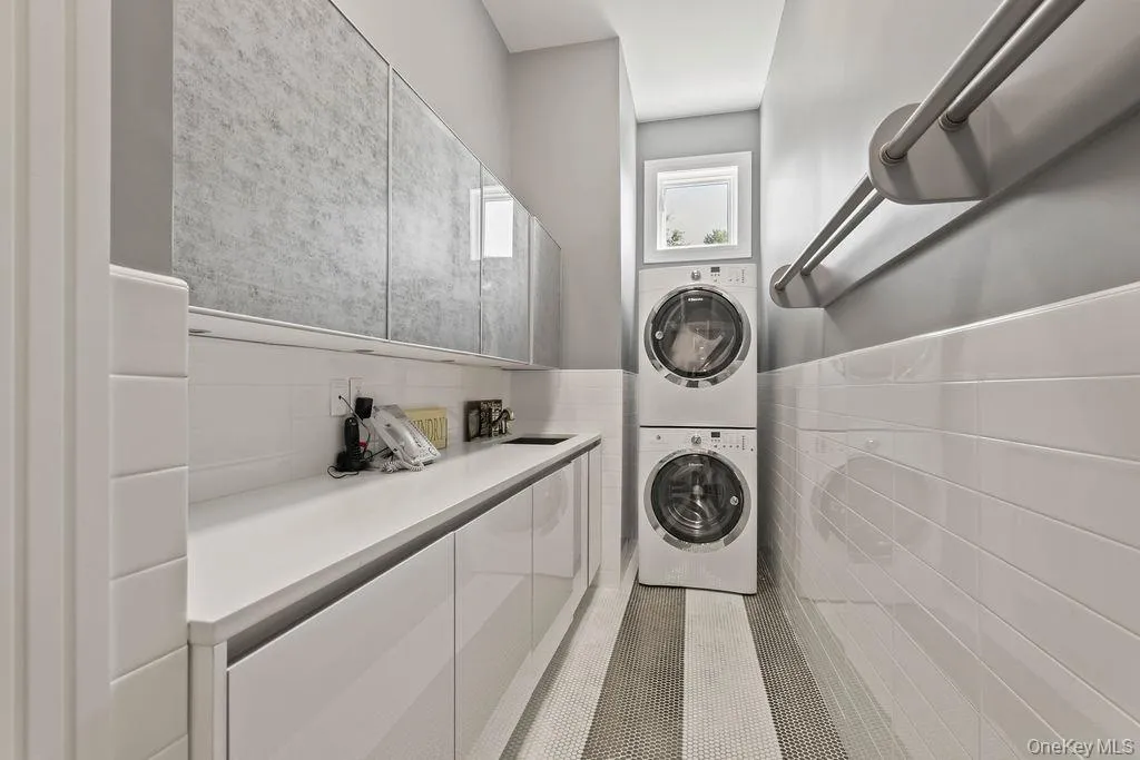 Dedicated utility area featuring a stacked washer and dryer, extensive countertop space, integrated sink, and upper cabinetry with textured paneling Dedicated utility area featuring a stacked washer and dryer, extensive countertop space, integrated sink, and upper cabinetry with textured paneling
