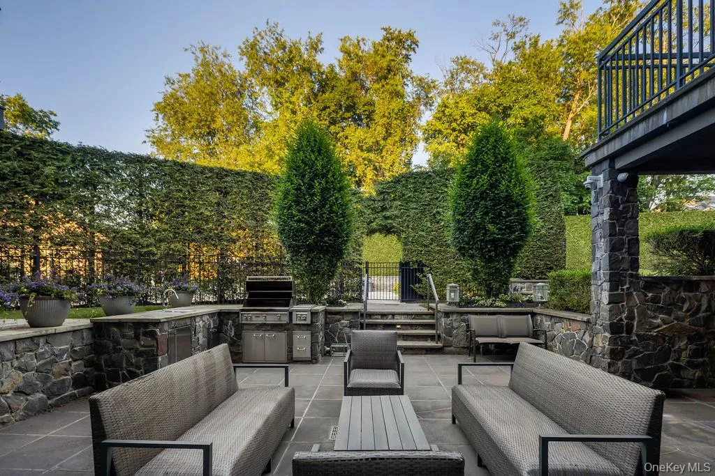 Outdoor patio featuring an integrated built-in grill station, stone-clad retaining walls, and a bluestone patio surface Outdoor patio featuring an integrated built-in grill station, stone-clad retaining walls, and a bluestone patio surface