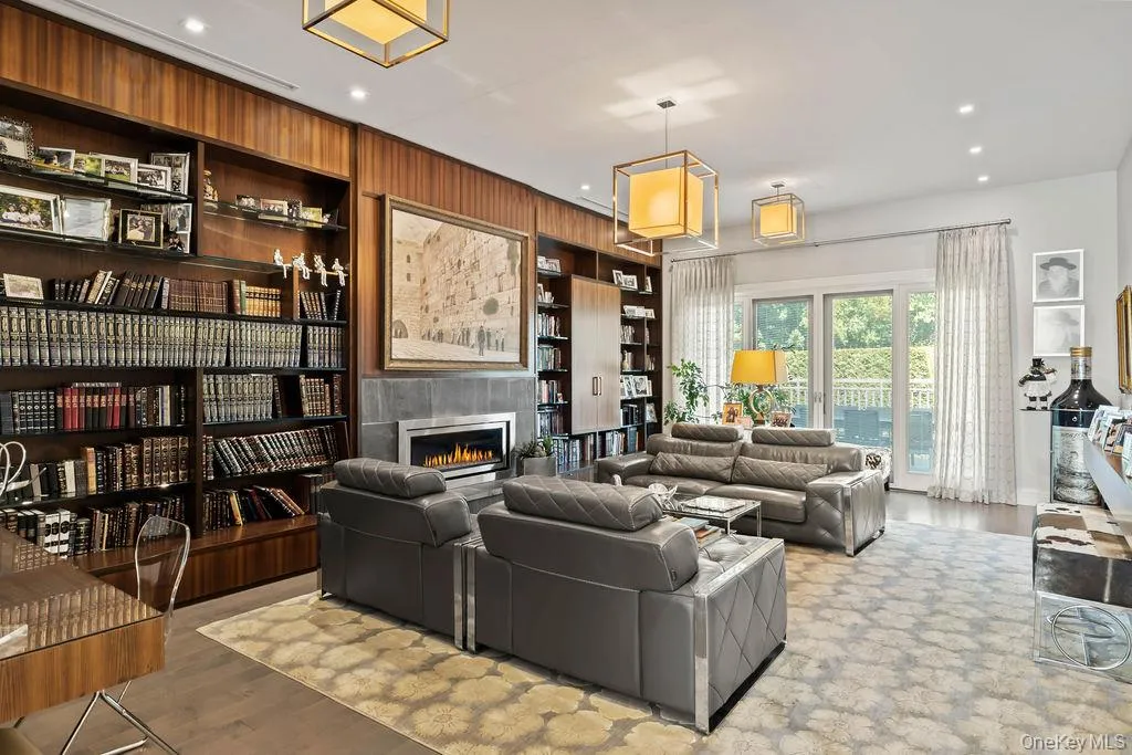 Wood-paneled library featuring extensive built-in shelving, a gas fireplace with a stone surround, recessed lighting, and elegant pendant light fixtures Wood-paneled library featuring extensive built-in shelving, a gas fireplace with a stone surround, recessed lighting, and elegant pendant light fixtures