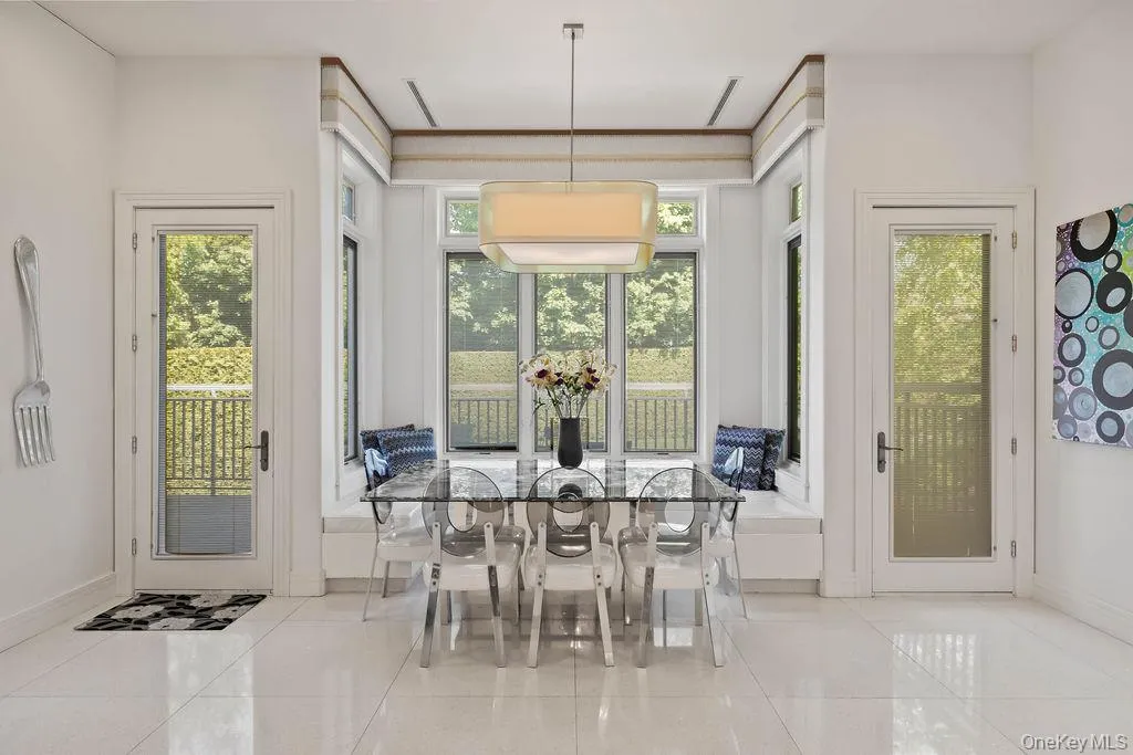 Bright dining area featuring a built-in window seat, large windows with garden railings, and two glass-paneled doors Bright dining area featuring a built-in window seat, large windows with garden railings, and two glass-paneled doors