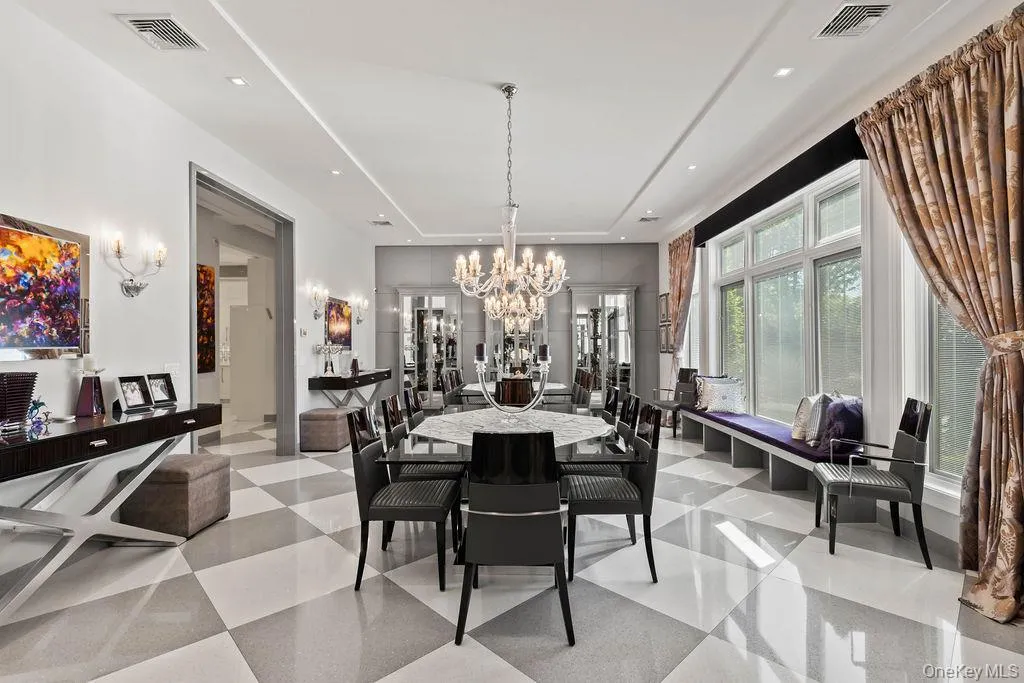 Spacious dining room featuring a large central chandelier, checkerboard tile flooring, a built-in window bench, and wall sconces Spacious dining room featuring a large central chandelier, checkerboard tile flooring, a built-in window bench, and wall sconces