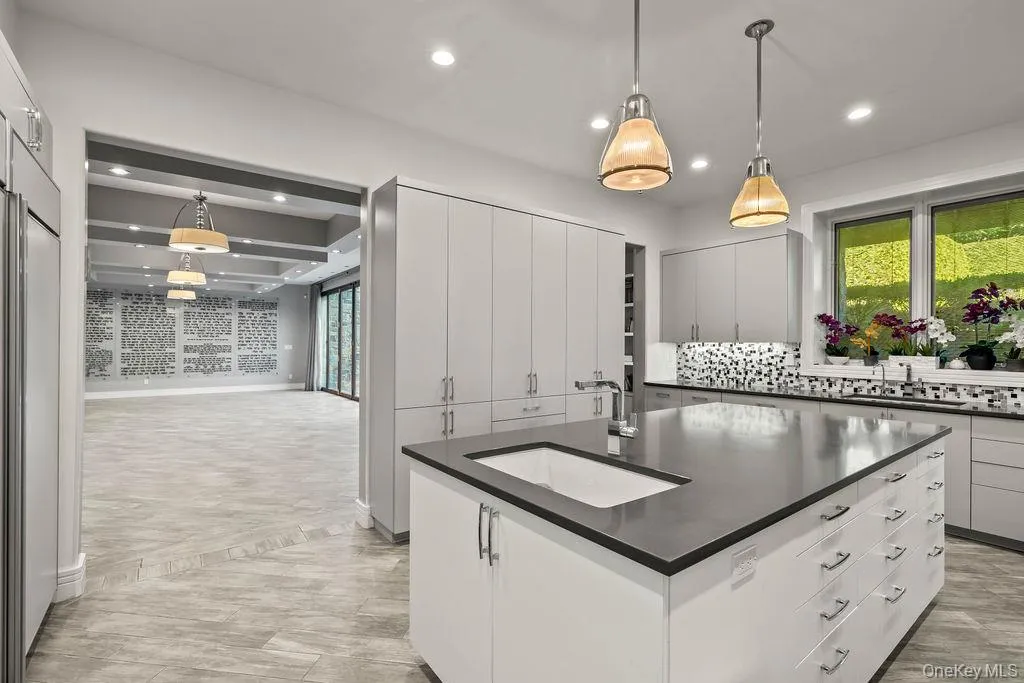 Spacious kitchen featuring an expansive center island with an integrated sink, white cabinetry, a mosaic tile backsplash, and recessed lighting Spacious kitchen featuring an expansive center island with an integrated sink, white cabinetry, a mosaic tile backsplash, and recessed lighting