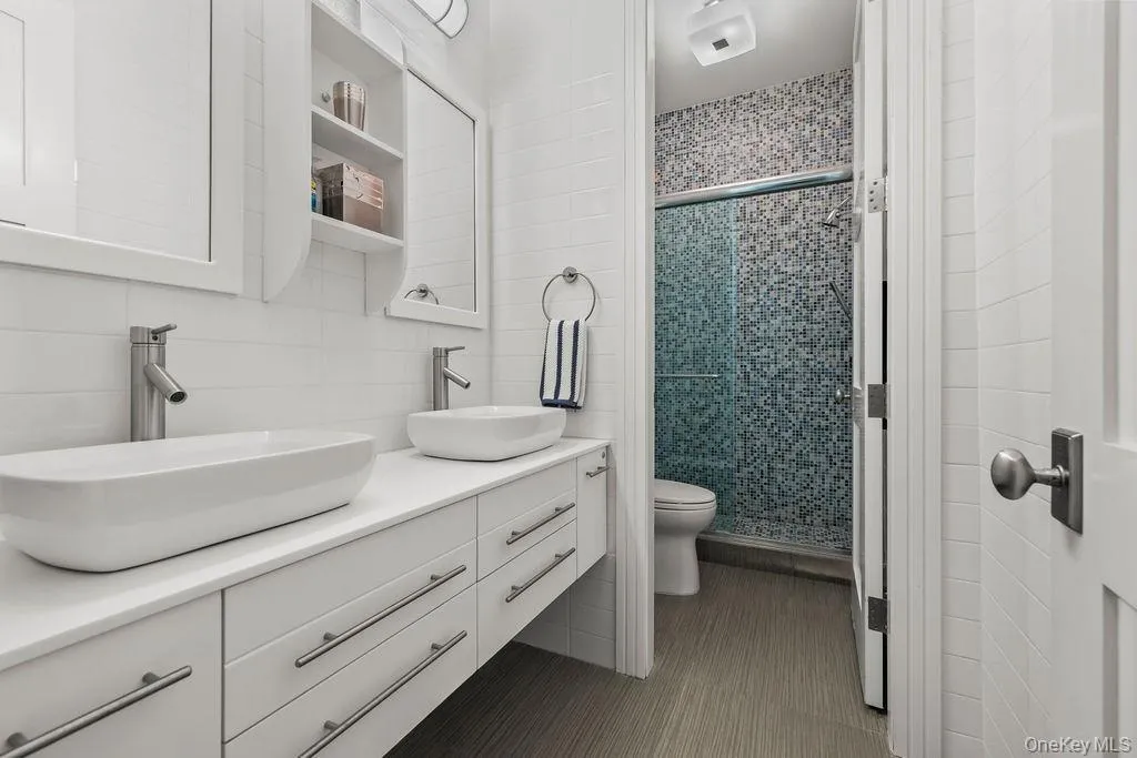 Contemporary bathroom featuring a double vanity with vessel sinks, white cabinetry, and brushed nickel hardware Contemporary bathroom featuring a double vanity with vessel sinks, white cabinetry, and brushed nickel hardware