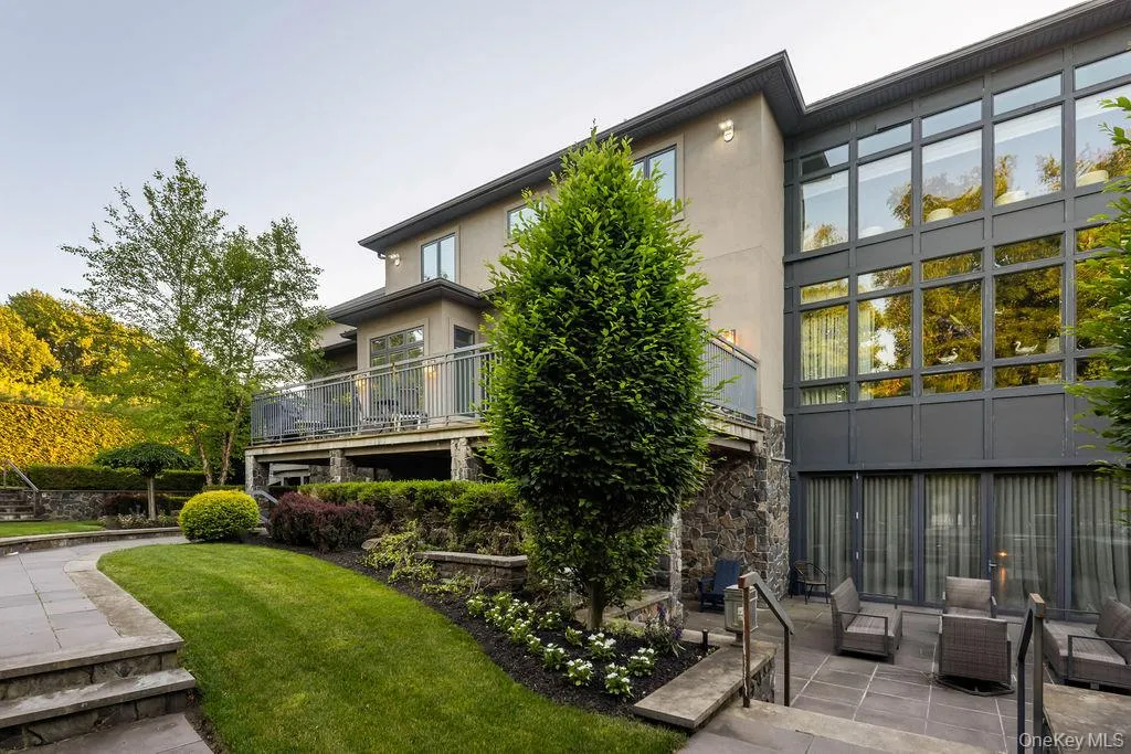 Rear stucco and stone veneer exterior featuring a large upper deck with metal railings, a full-height window wall, and a lower stone patio Rear stucco and stone veneer exterior featuring a large upper deck with metal railings, a full-height window wall, and a lower stone patio