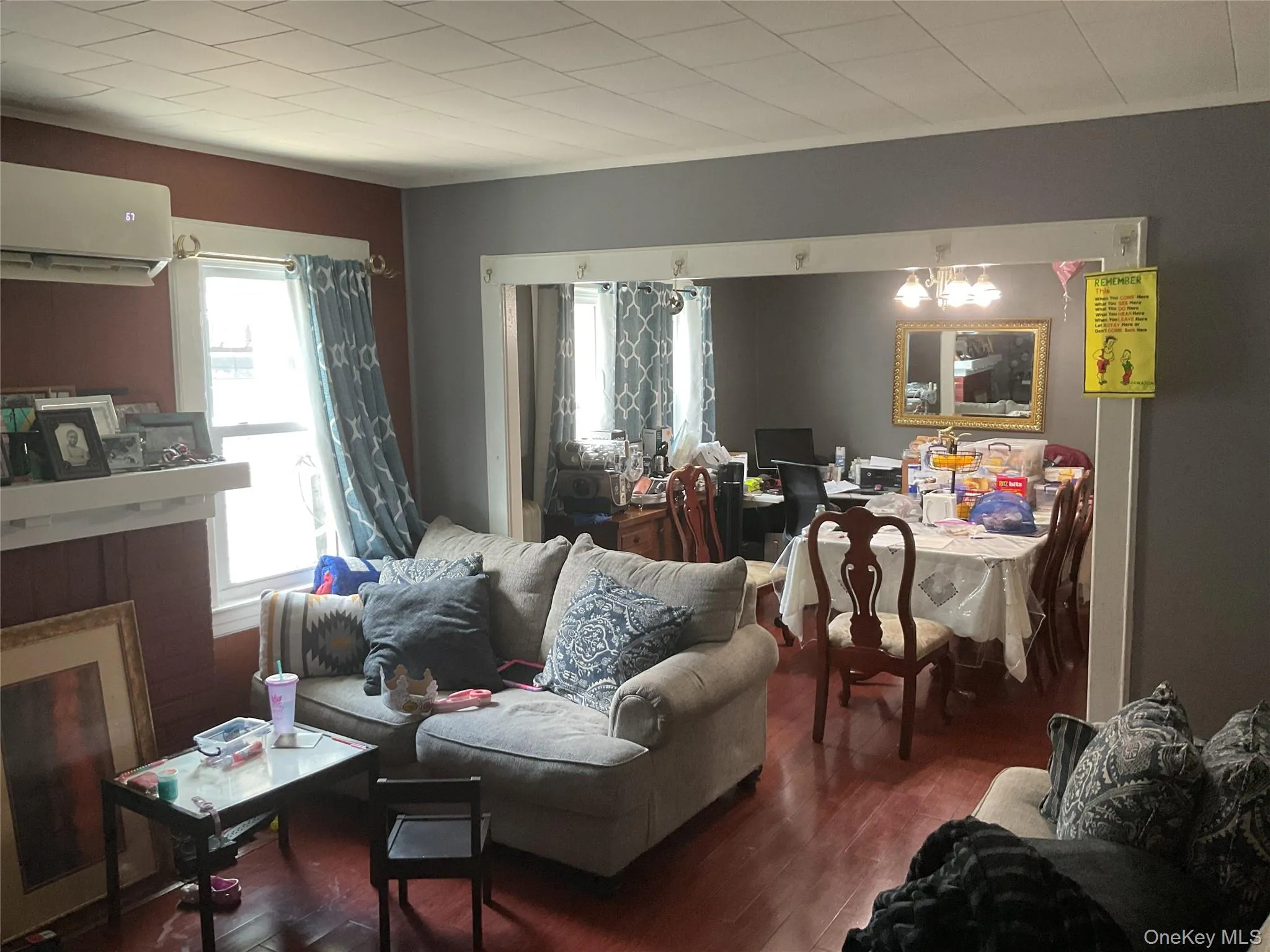 Living area featuring wood-finish flooring, a white mantel, and a wall-mounted air conditioning unit Living area featuring wood-finish flooring, a white mantel, and a wall-mounted air conditioning unit