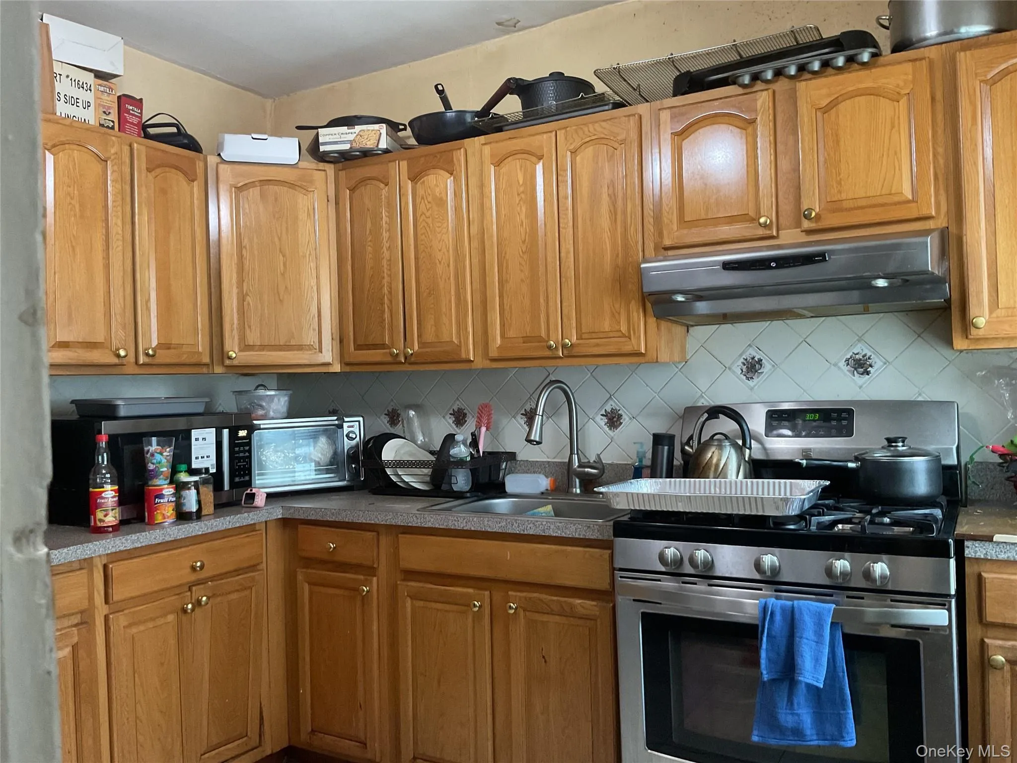 Kitchen featuring light wood cabinetry with gold-tone hardware, a stainless steel range, and a coordinating range hood Kitchen featuring light wood cabinetry with gold-tone hardware, a stainless steel range, and a coordinating range hood