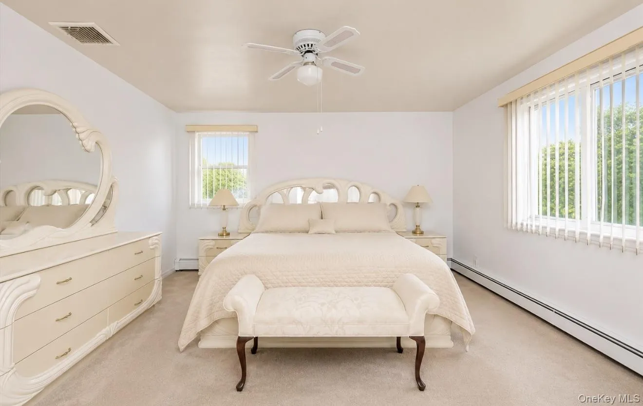 Bright Master bedroom Ensuite featuring two windows with vertical blinds, a ceiling fan, and light-toned carpet, jack & jill bath Bright Master bedroom Ensuite featuring two windows with vertical blinds, a ceiling fan, and light-toned carpet, jack & jill bath