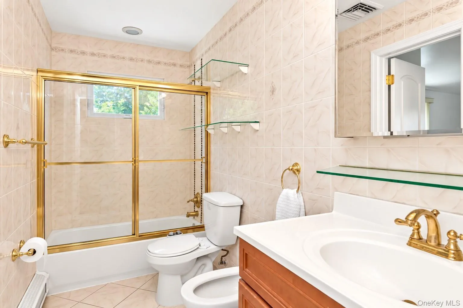 Ceramic tile walls and flooring, brass-finish fixtures, single vanity with integrated sink, and glass shower enclosure Ceramic tile walls and flooring, brass-finish fixtures, single vanity with integrated sink, and glass shower enclosure