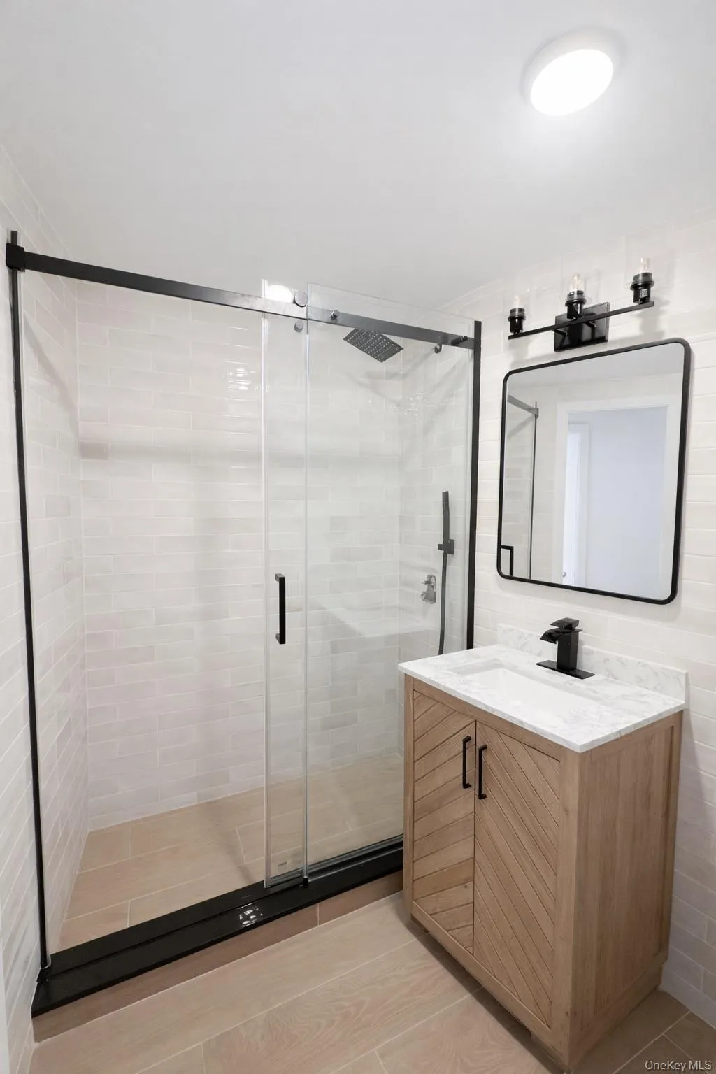 Contemporary bathroom featuring a glass-enclosed shower with black trim, a square rainfall showerhead, and light-toned tile flooring Contemporary bathroom featuring a glass-enclosed shower with black trim, a square rainfall showerhead, and light-toned tile flooring