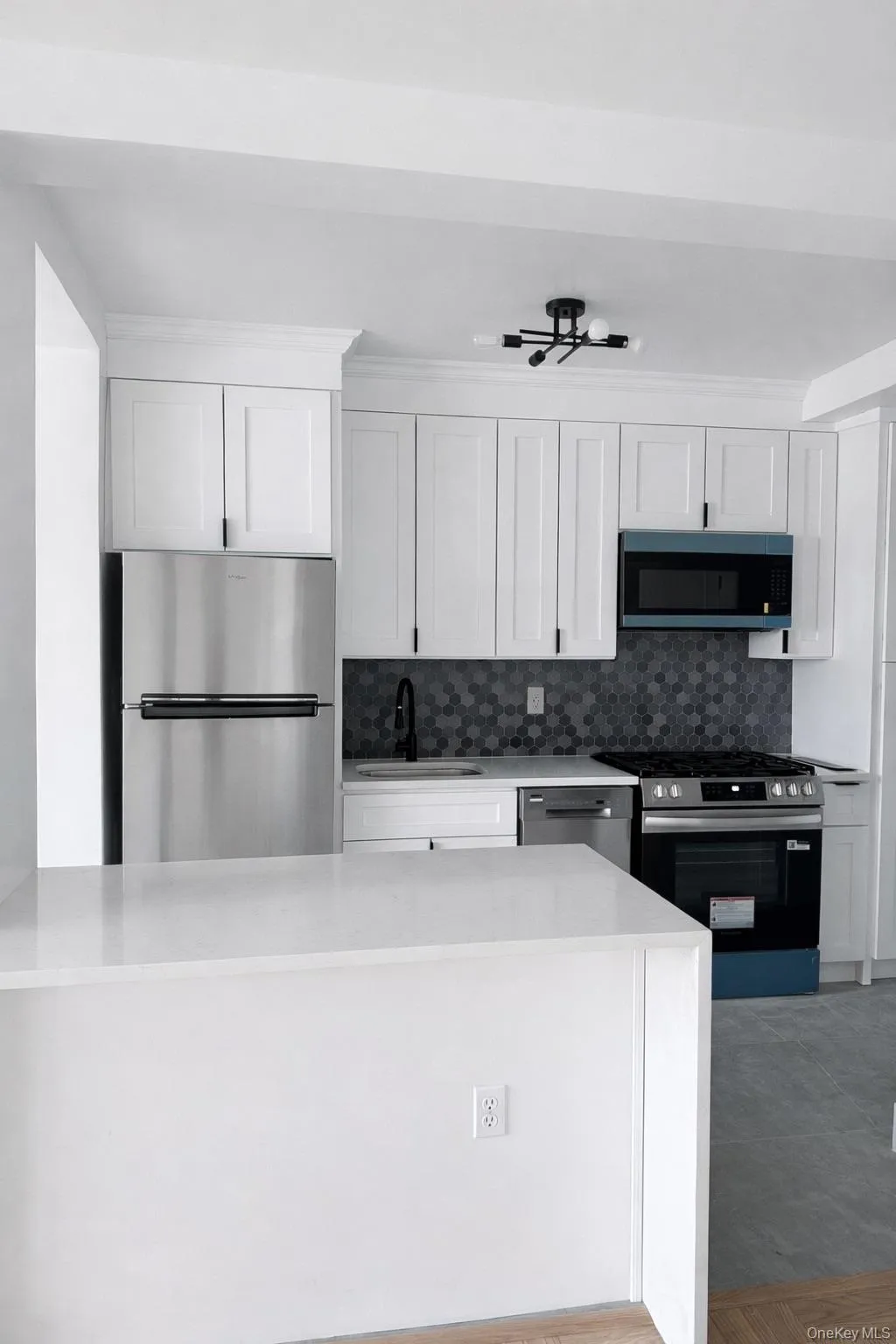 Modern kitchen featuring white shaker cabinetry, stainless steel appliances, a dark hexagonal tile backsplash, and a white countertop peninsula Modern kitchen featuring white shaker cabinetry, stainless steel appliances, a dark hexagonal tile backsplash, and a white countertop peninsula
