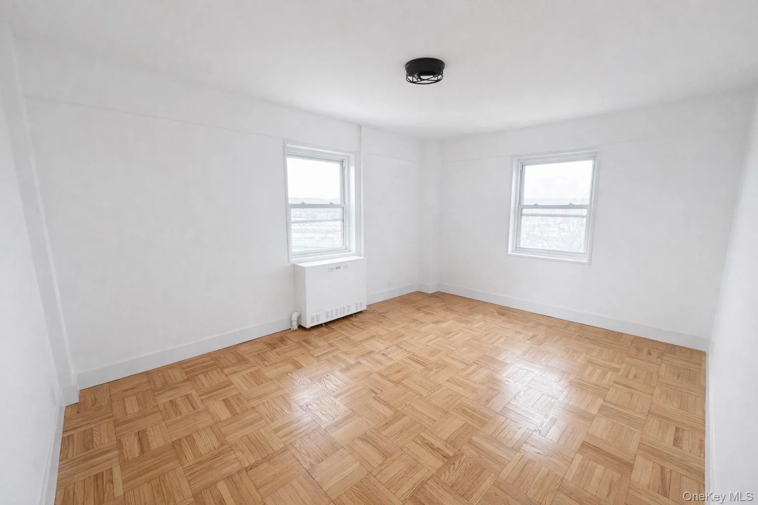 Bright interior space featuring parquet wood-finish flooring, white baseboards, and two double-hung windows Bright interior space featuring parquet wood-finish flooring, white baseboards, and two double-hung windows