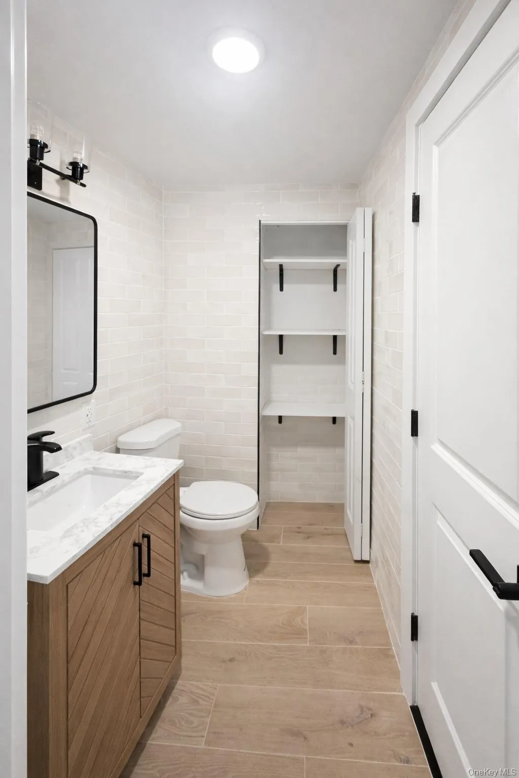 Bathroom featuring a wood-finish vanity with a white countertop and rectangular undermount sink, a matte black faucet, and a black-framed rectangular mirror. Bathroom featuring a wood-finish vanity with a white countertop and rectangular undermount sink, a matte black faucet, and a black-framed rectangular mirror.