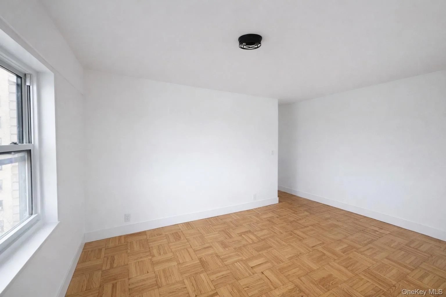 Expansive room featuring parquet wood flooring, white painted walls, and a single window with a white frame Expansive room featuring parquet wood flooring, white painted walls, and a single window with a white frame