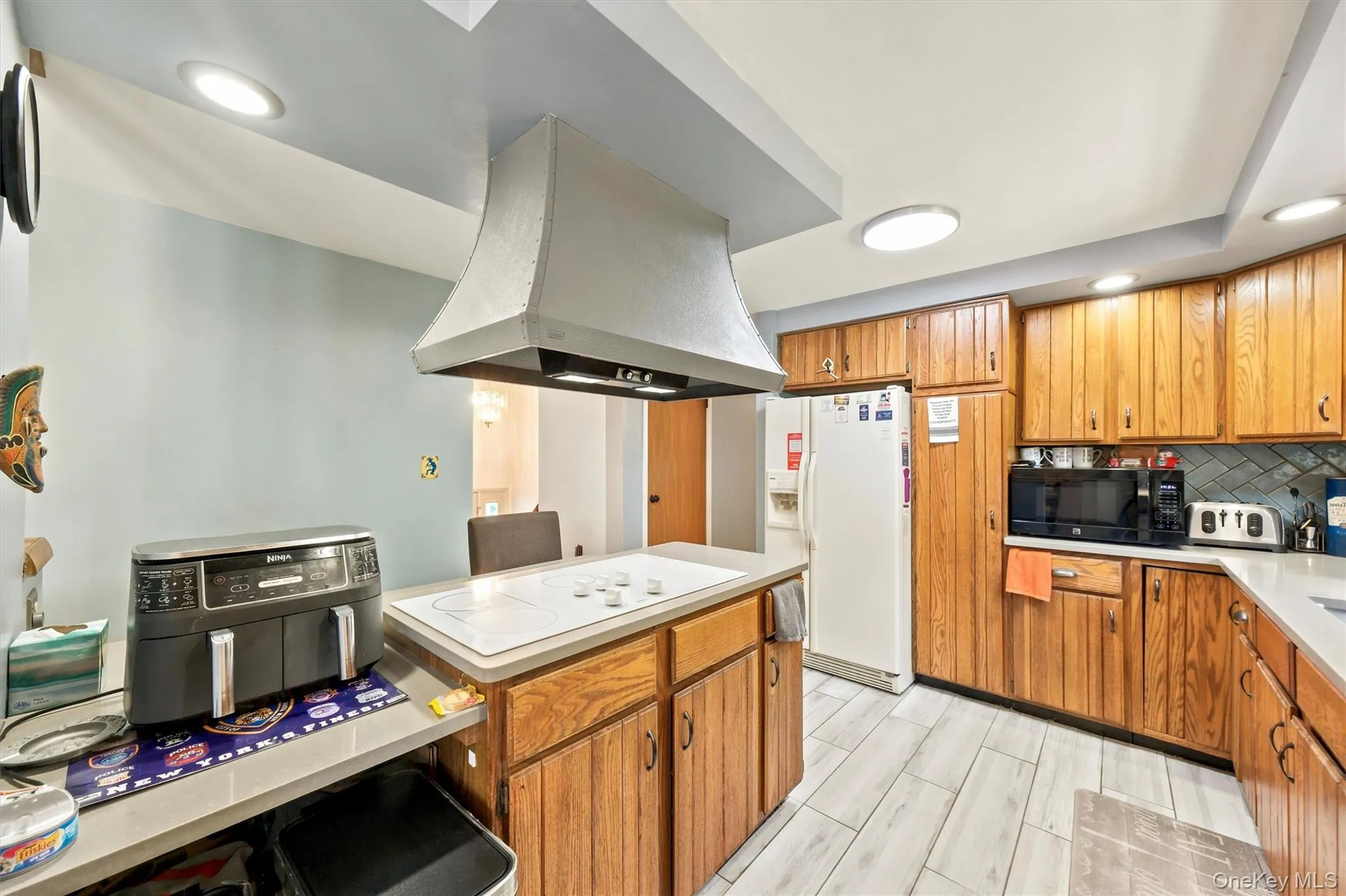 Kitchen featuring wood-finish cabinetry, light-toned countertops, and a built-in cooktop with an overhead range hood Kitchen featuring wood-finish cabinetry, light-toned countertops, and a built-in cooktop with an overhead range hood