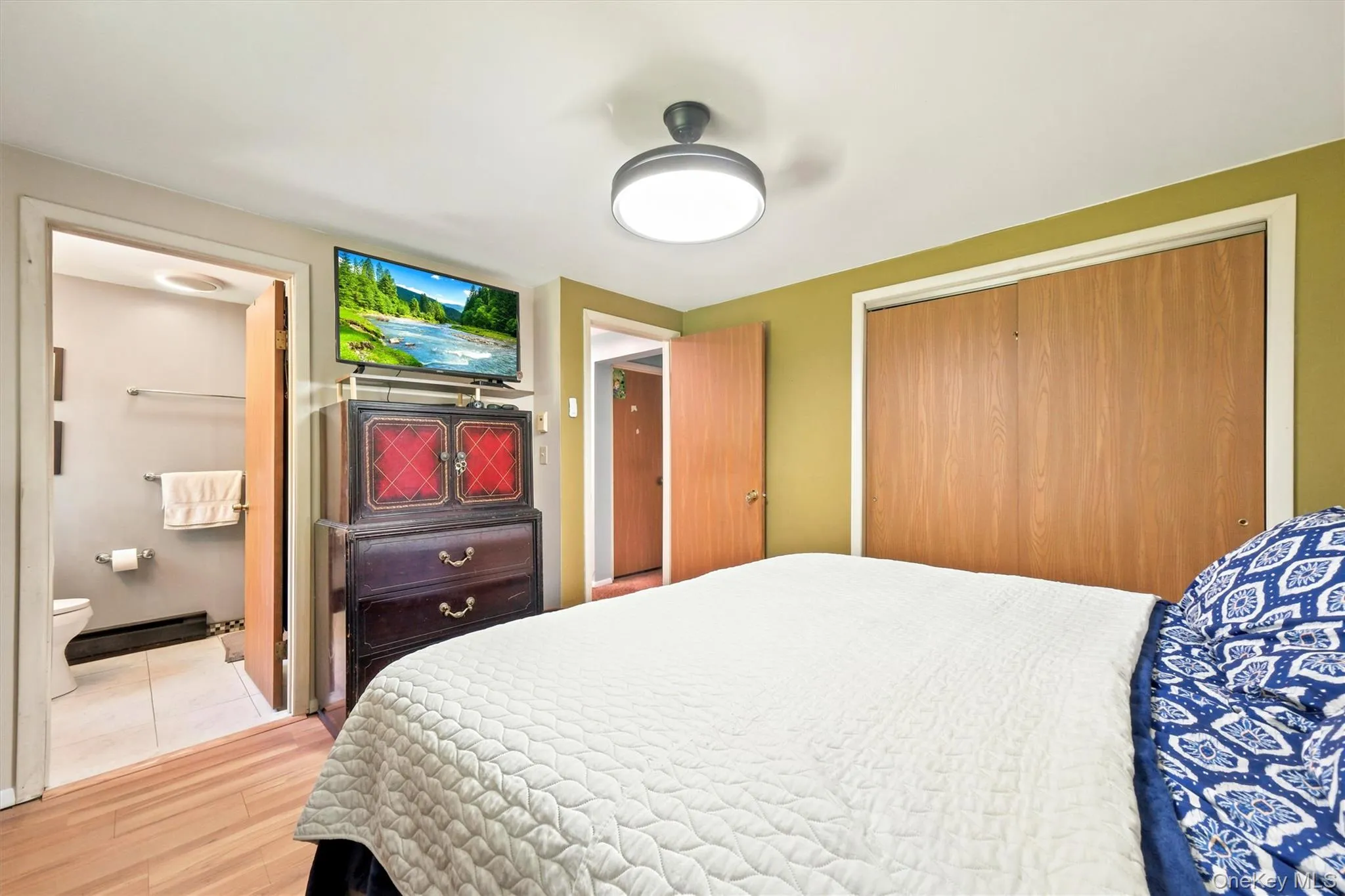 Bedroom featuring wood-finish flooring, a ceiling-mounted light fixture, and two panel closet doors Bedroom featuring wood-finish flooring, a ceiling-mounted light fixture, and two panel closet doors